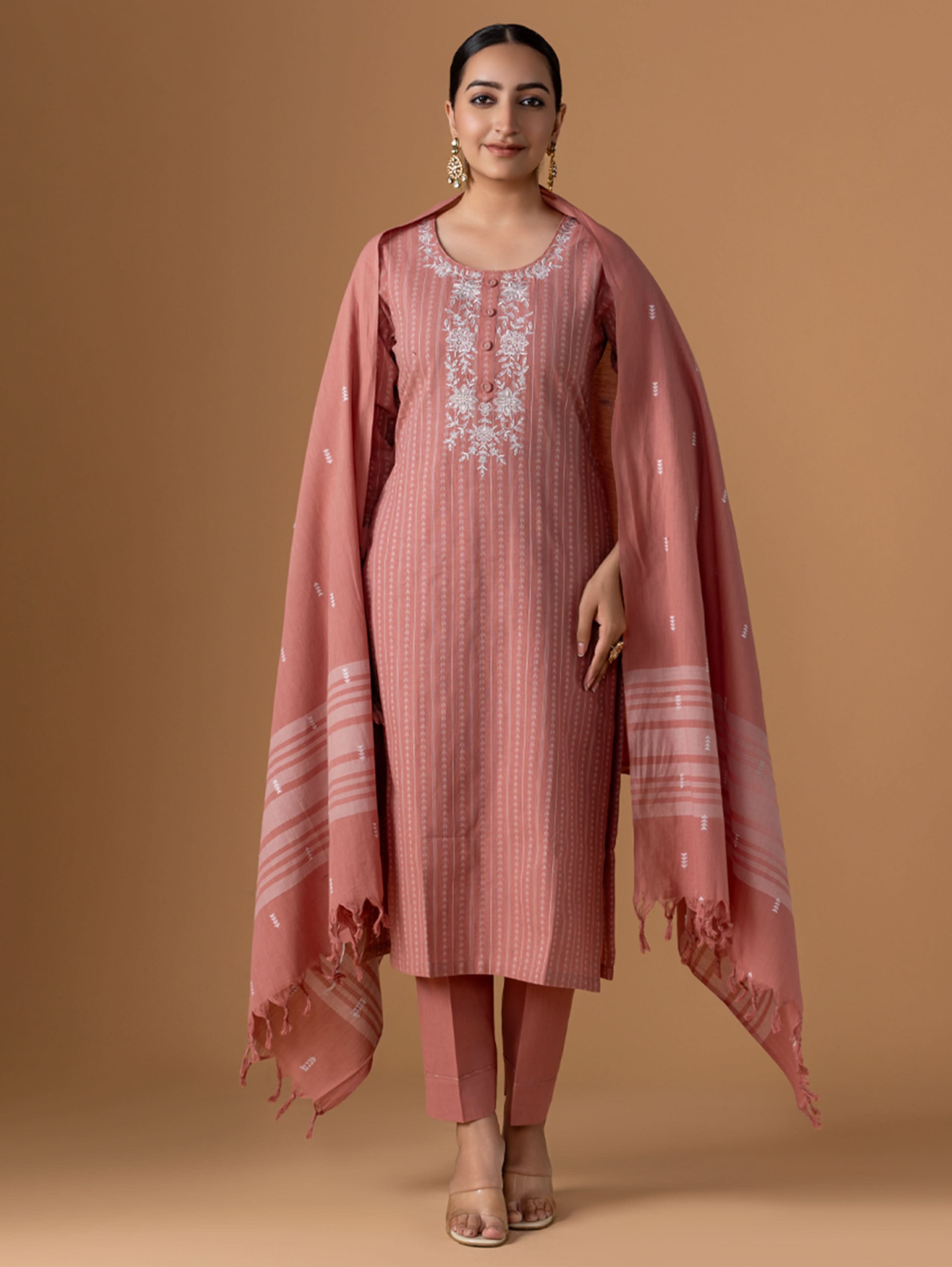A model wearing a pink Jamdani Pure Cotton suit set with embroidery on the kurta, consisting of a kurta, pants, and a dupatta.