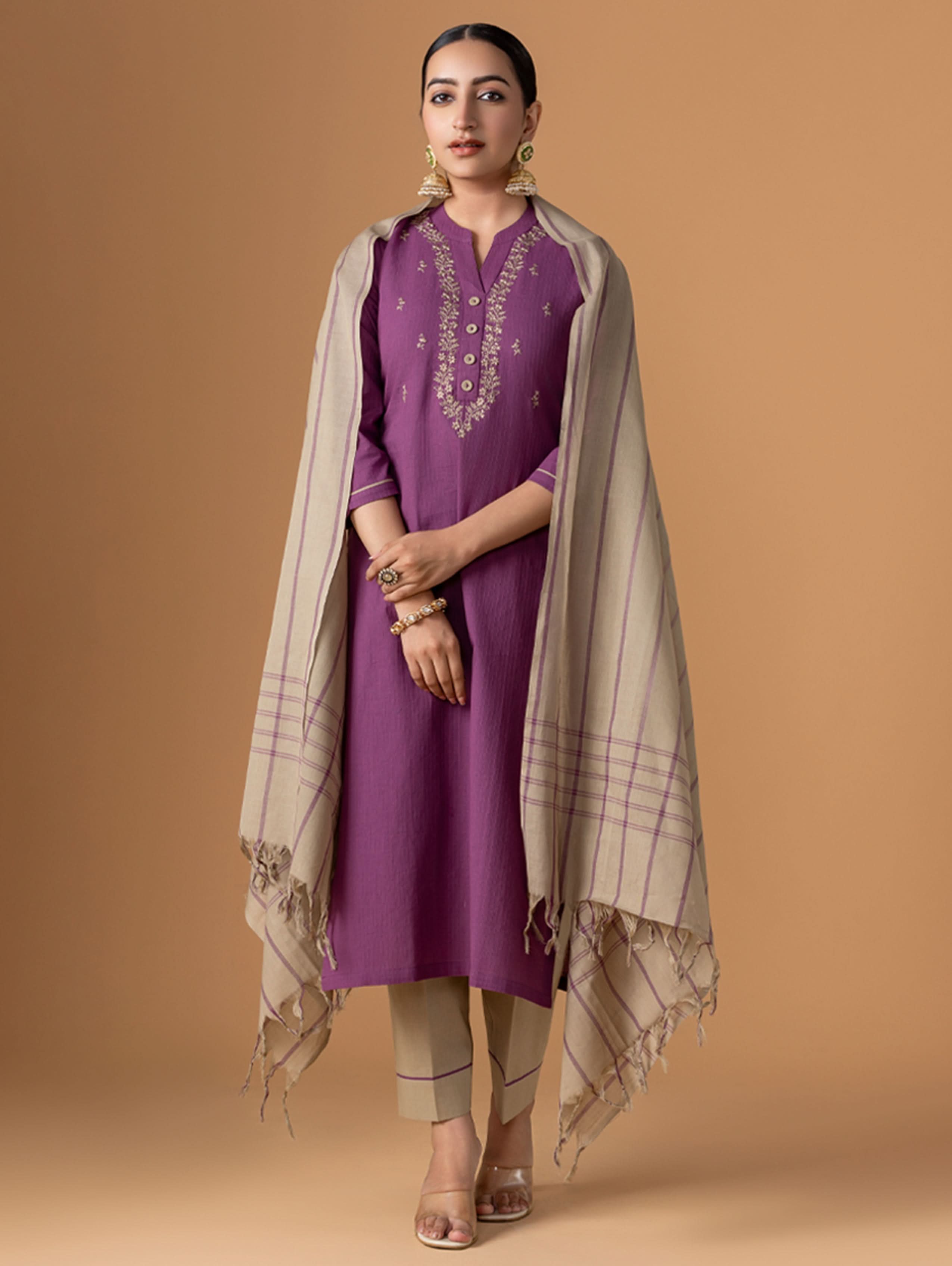 Woman wearing a purple outfit with a beige scarf against a brown background