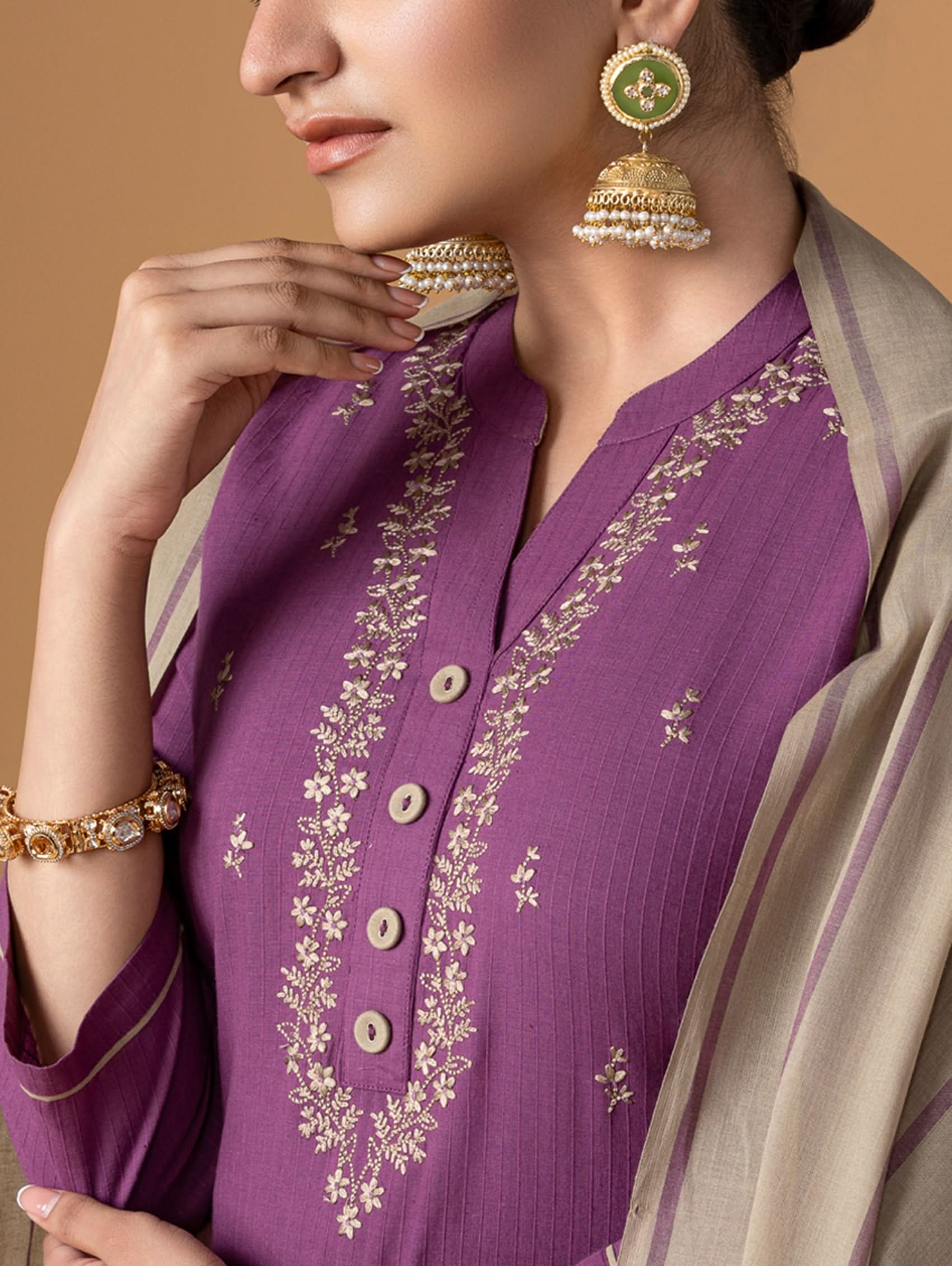 Woman wearing a purple embroidered outfit with gold details on a beige background
