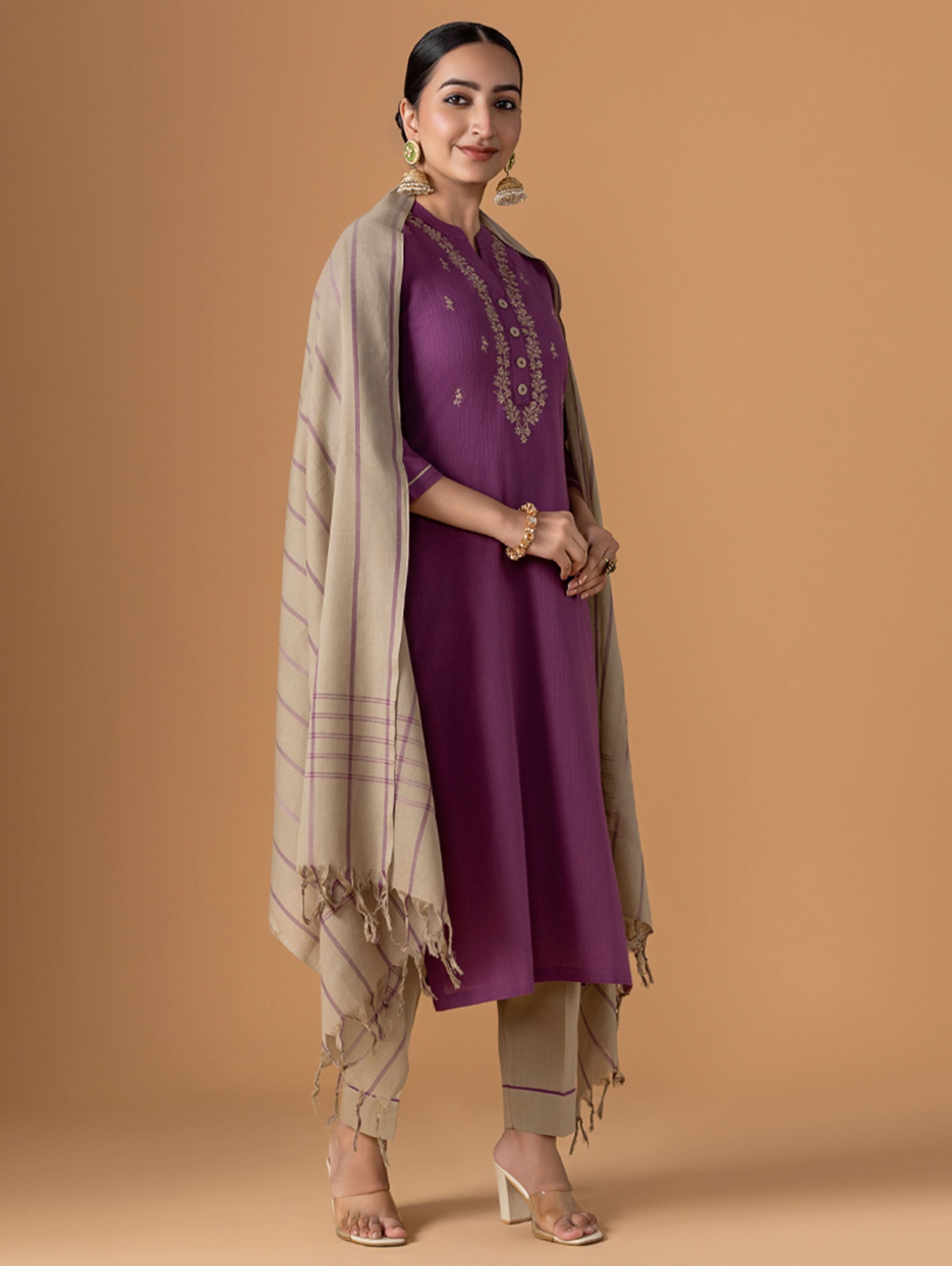 Woman wearing a purple outfit with a beige scarf against a brown background