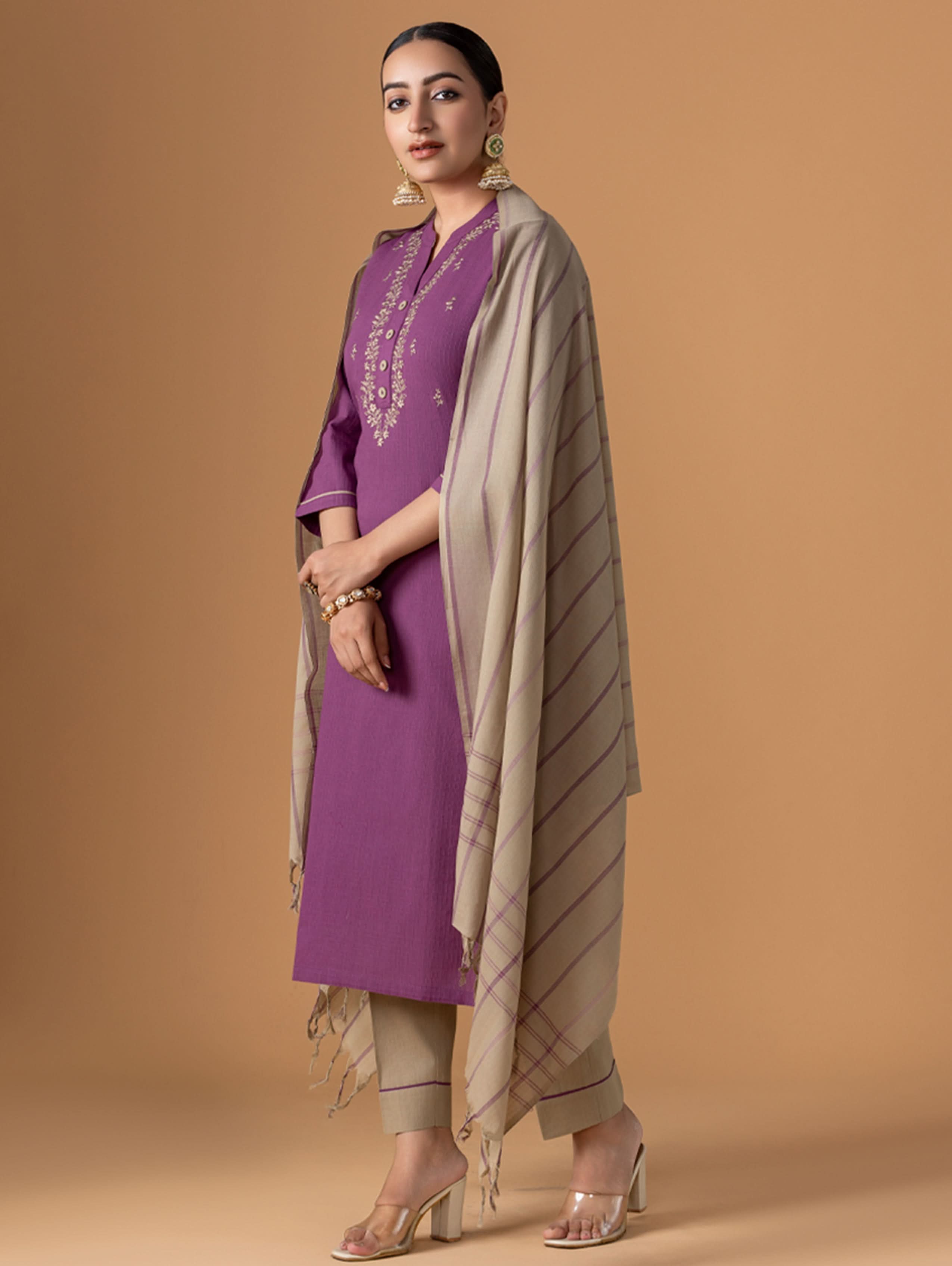 Woman wearing a purple outfit with a beige scarf against a brown background