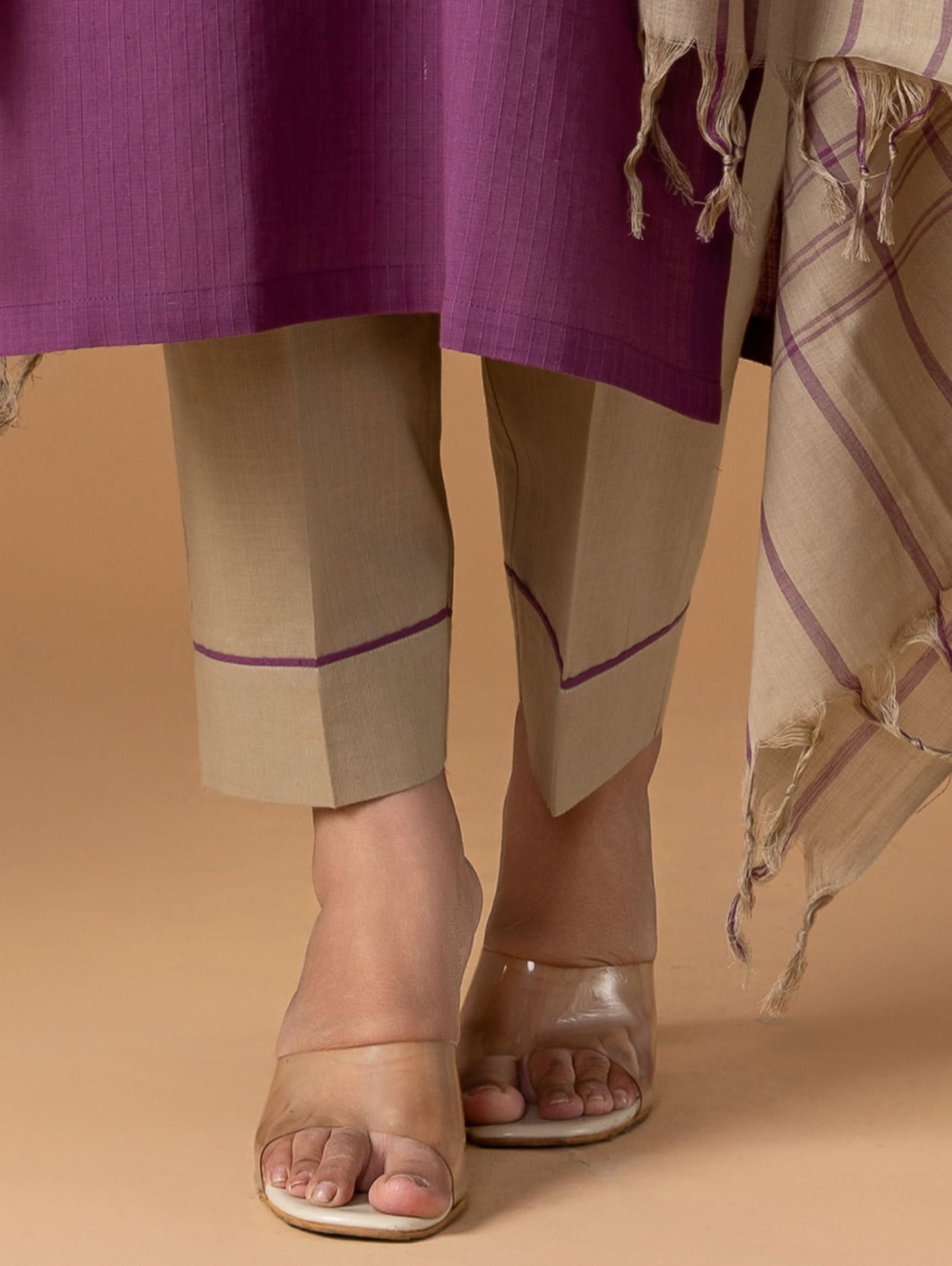 Person wearing a purple top and beige pants with a beige background