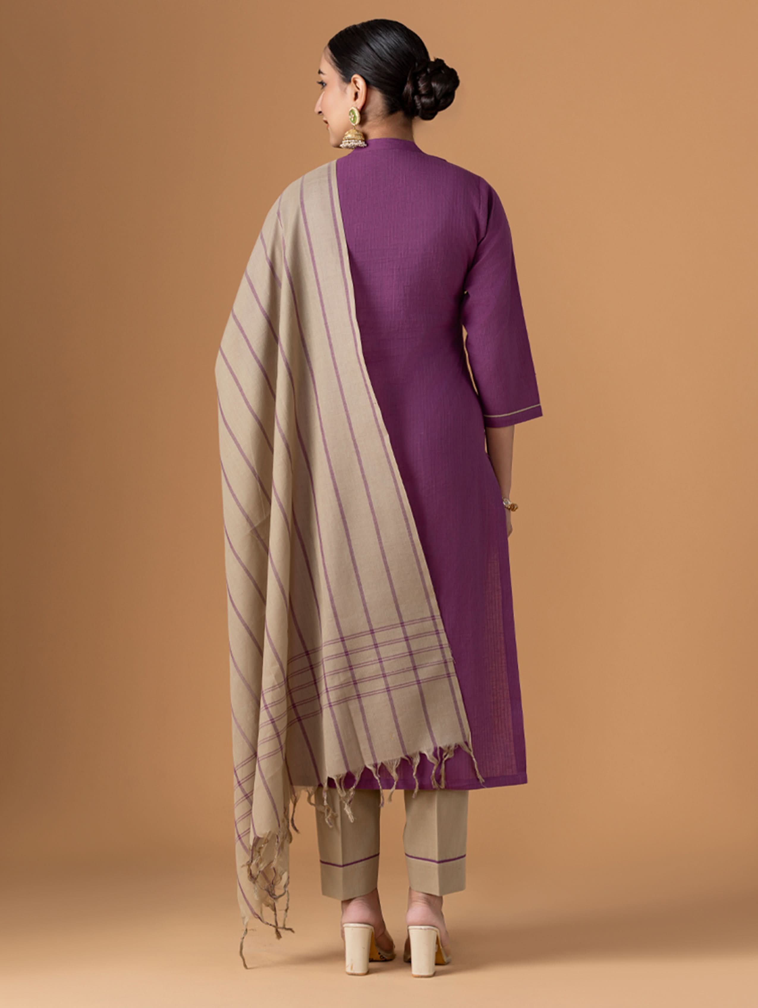 Woman wearing a purple kurta with a beige and brown striped dupatta on a beige background