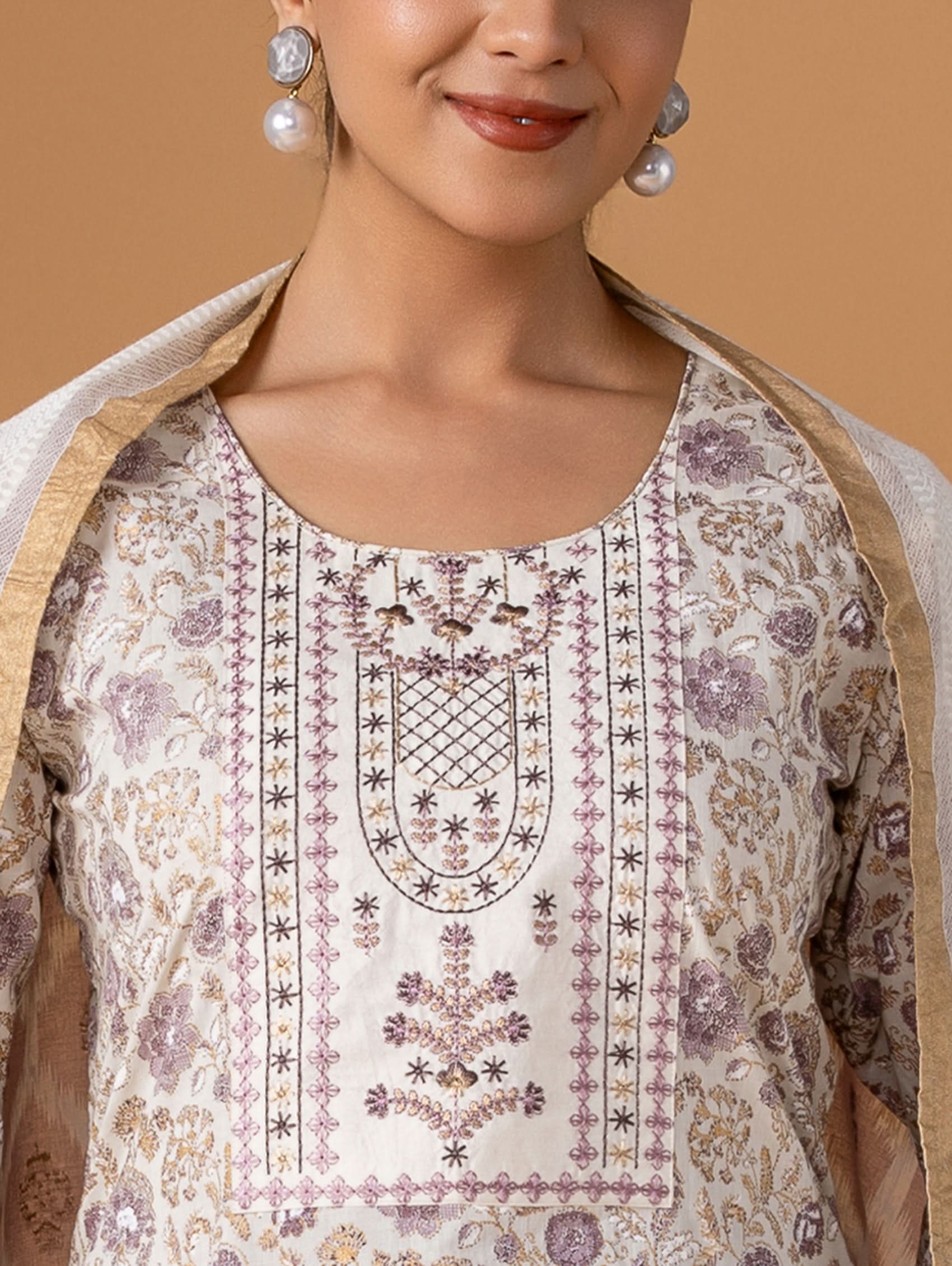 Woman wearing a traditional embroidered outfit with a beige shawl on a brown background