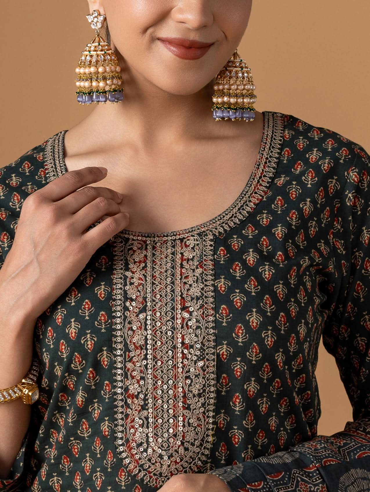 Woman wearing a patterned top with gold earrings against a beige background