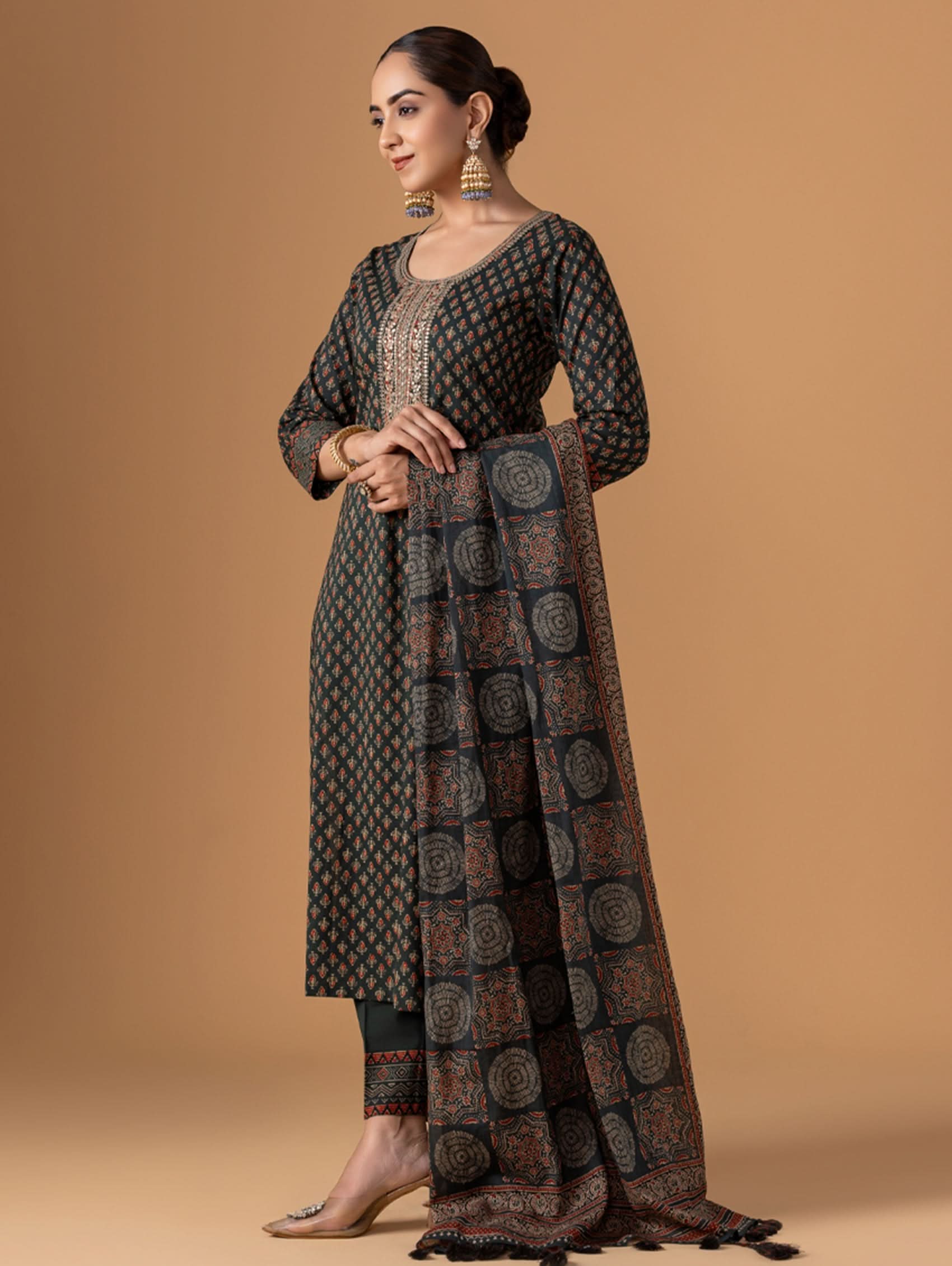 Woman wearing a traditional outfit with a patterned dress and dupatta against a beige background