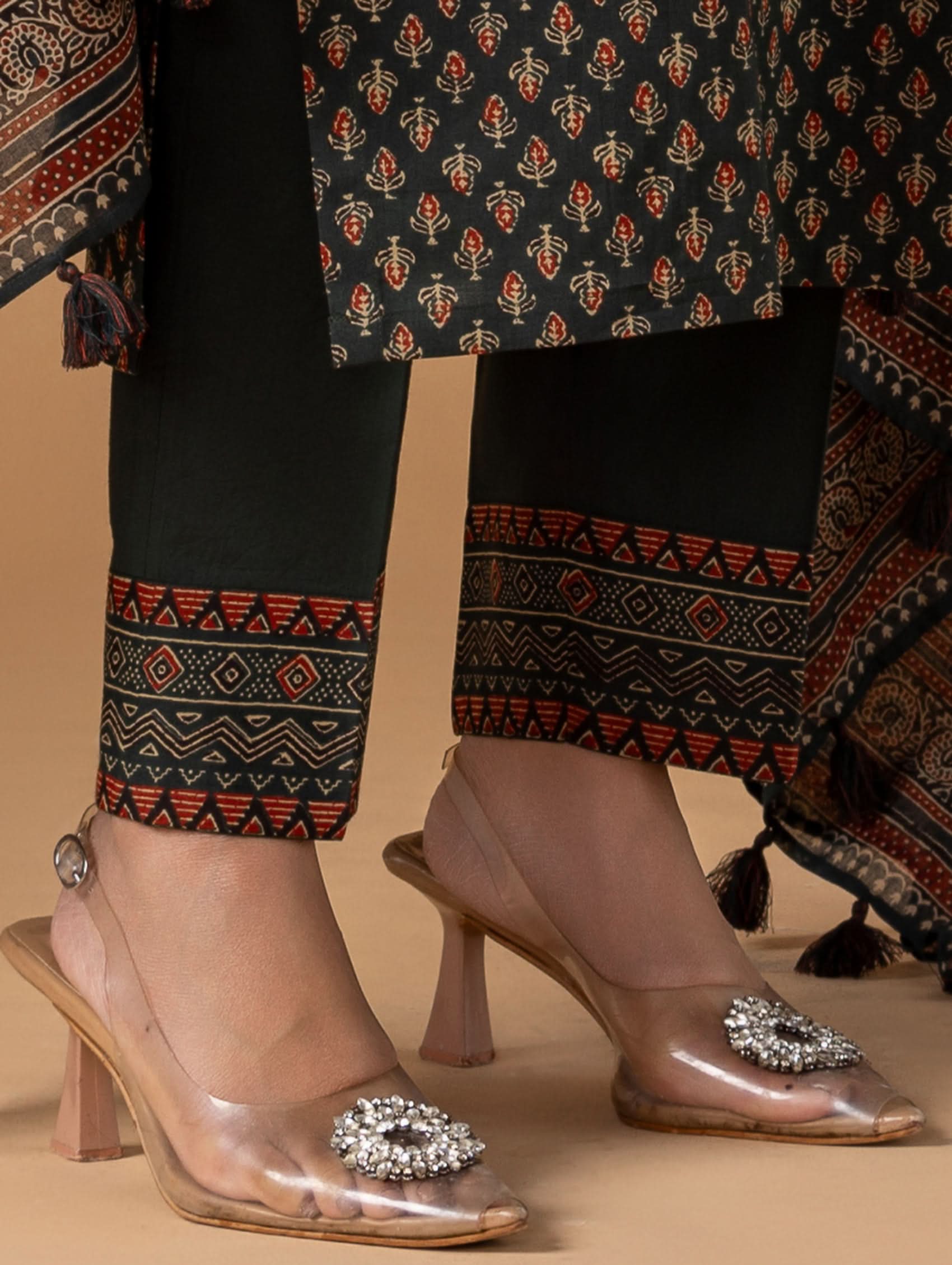 Patterned outfit with black pants and brown shoes on a beige background