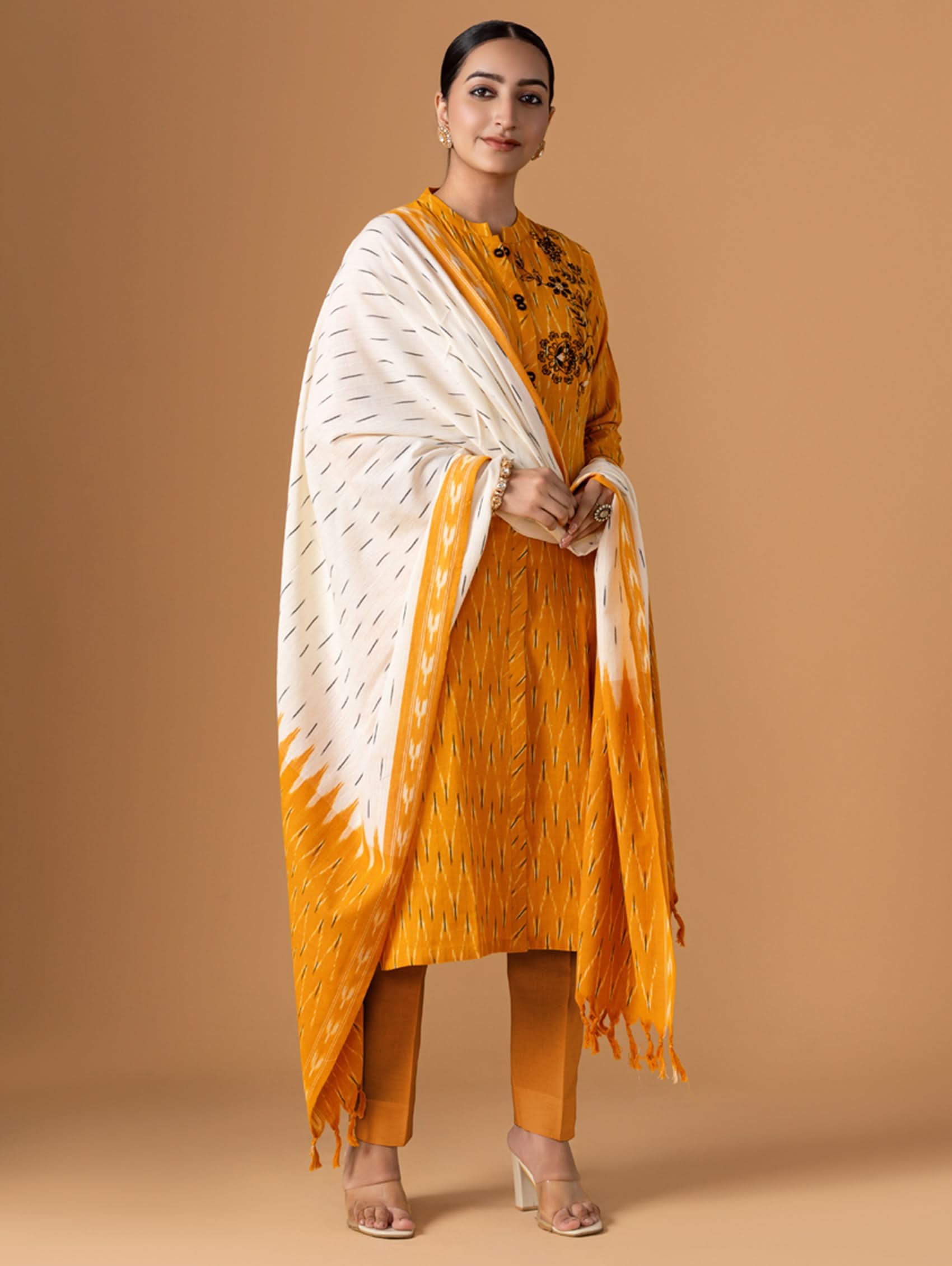 Woman wearing a mustard yellow outfit with a white shawl on a beige background