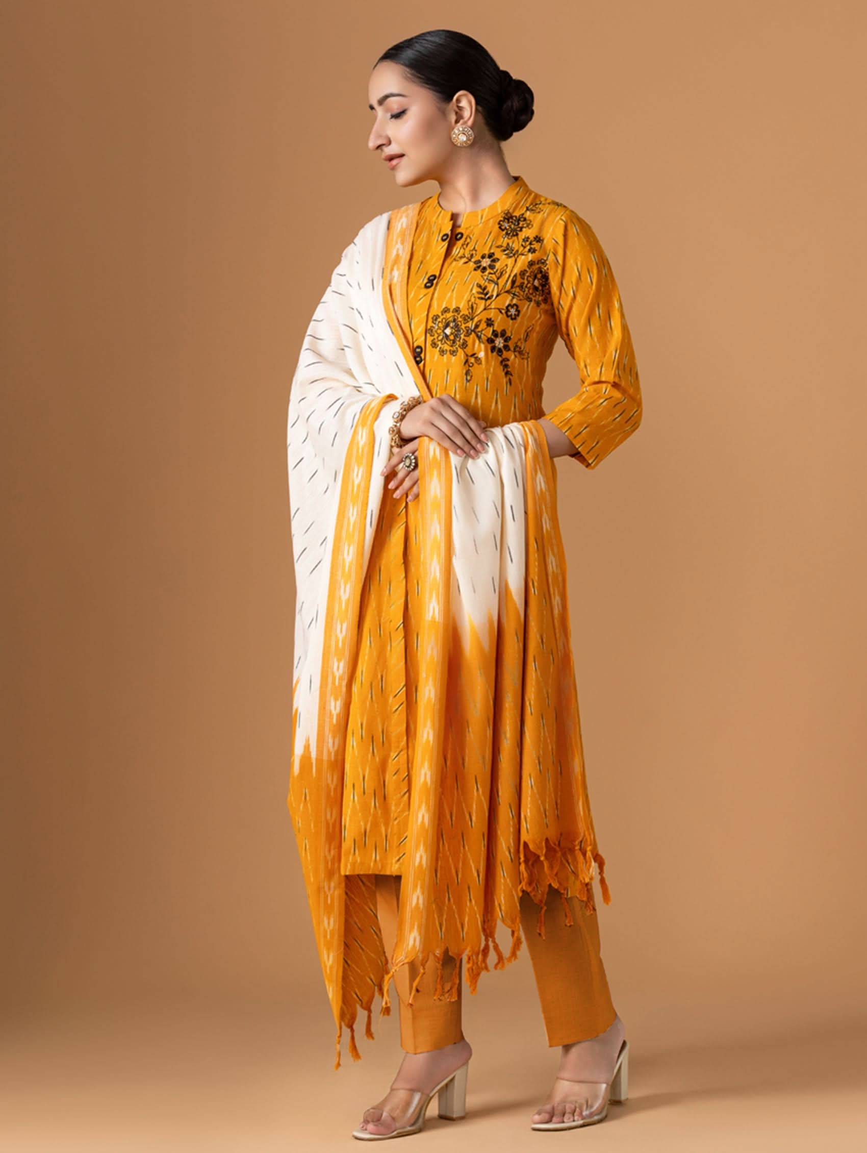 Woman wearing a traditional outfit with a yellow and white dress against a beige background