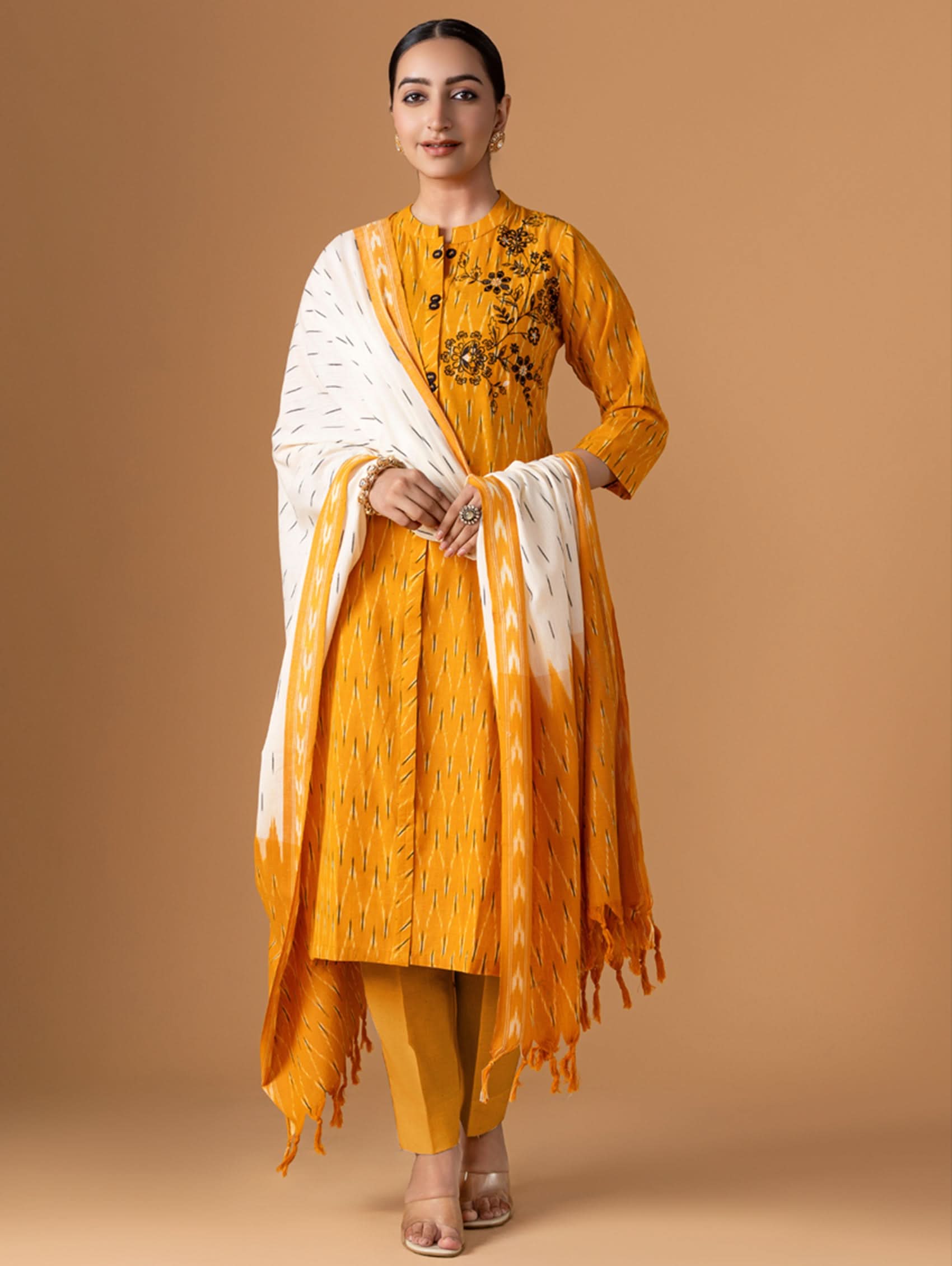 Woman wearing a mustard yellow traditional outfit with a white shawl on a brown background