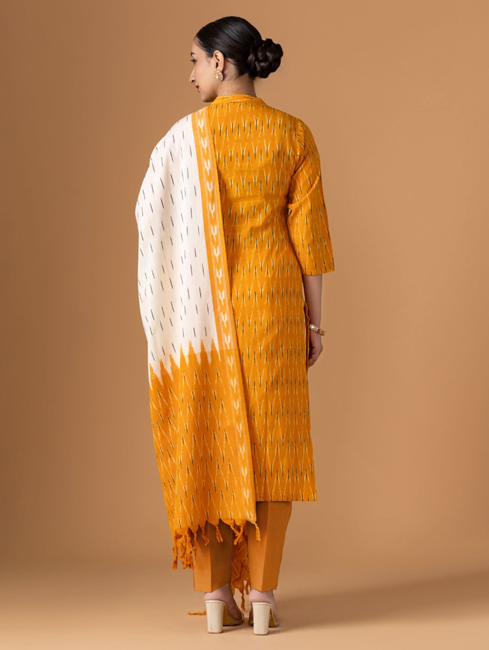 Woman wearing a mustard yellow and white patterned kurta with a matching dupatta on a beige background