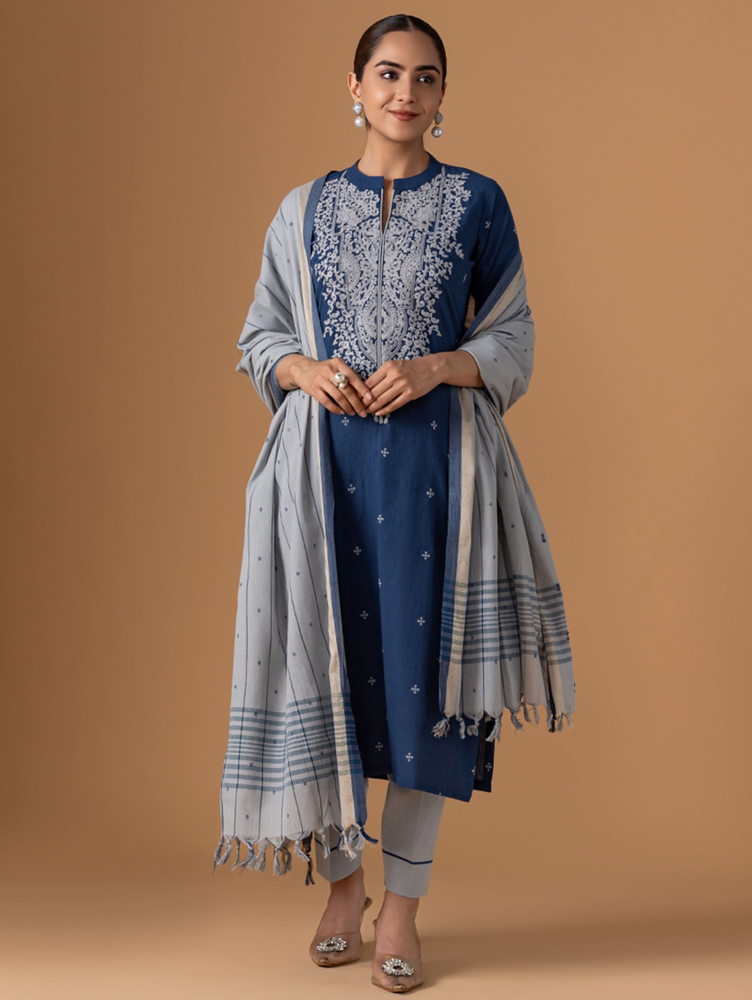 Woman wearing a blue embroidered kurta with a matching dupatta on a brown background