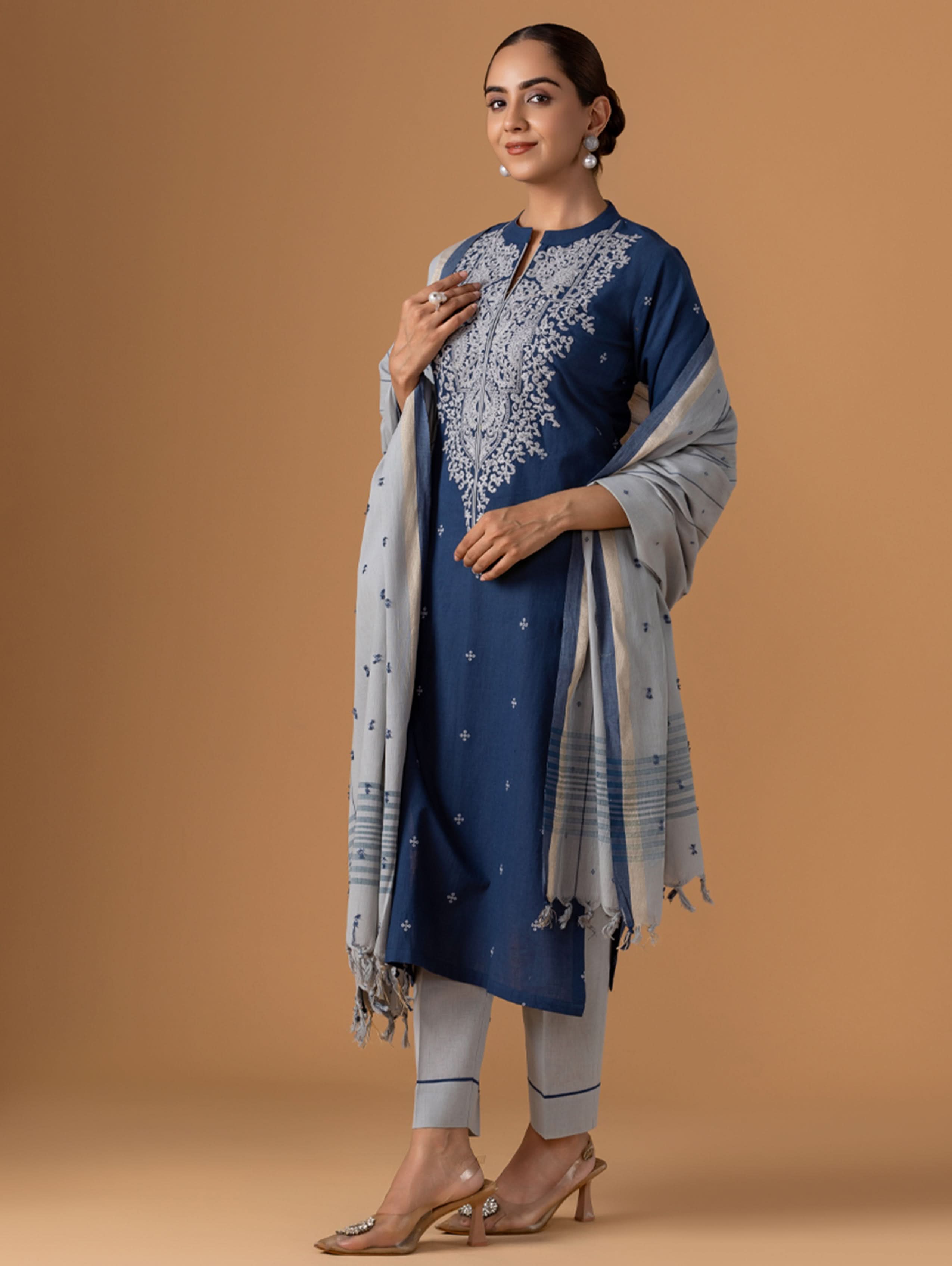Woman wearing a blue embroidered outfit with a matching shawl on a brown background