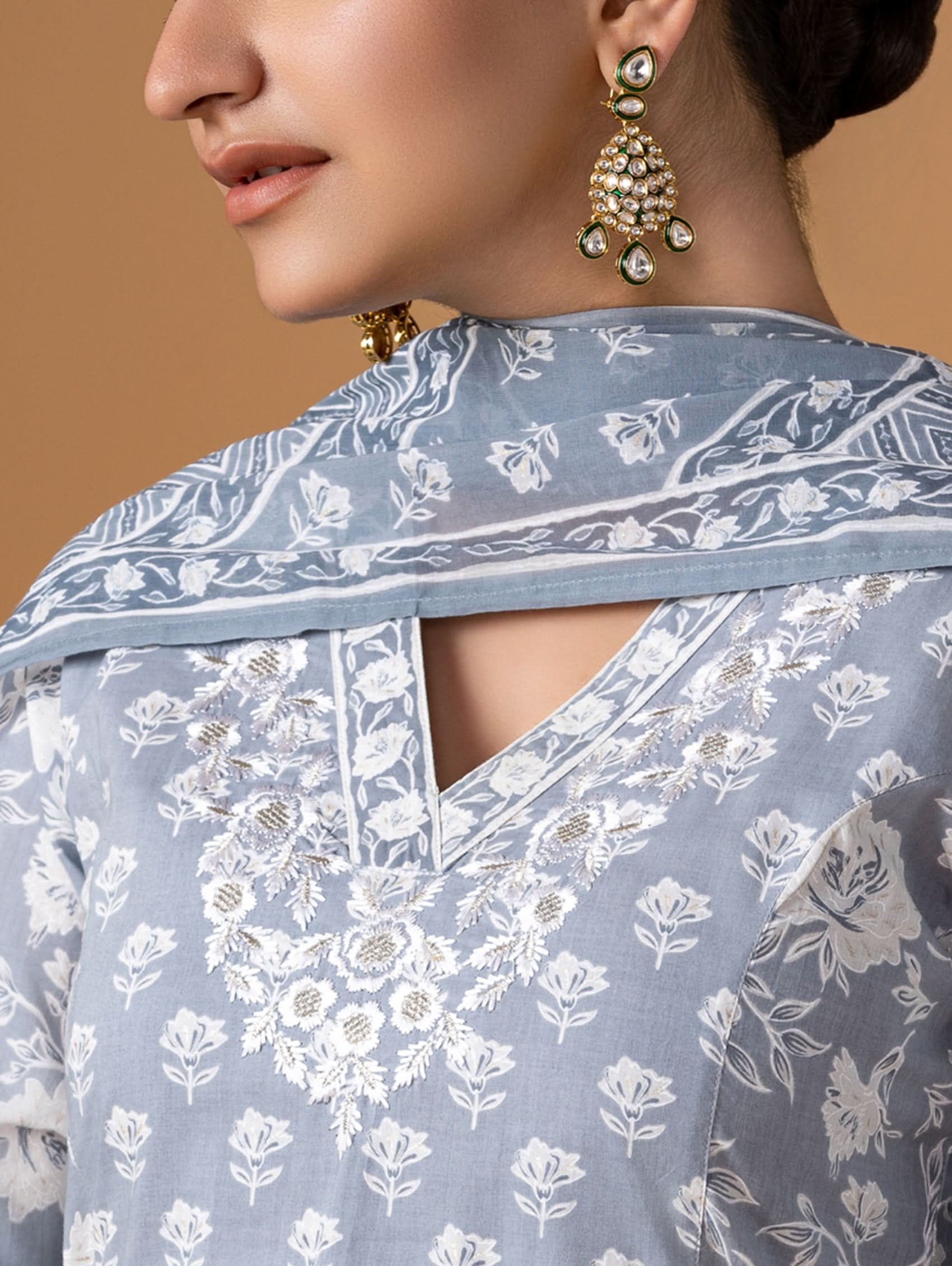 Woman wearing a light blue floral saree with gold jewelry against a beige background