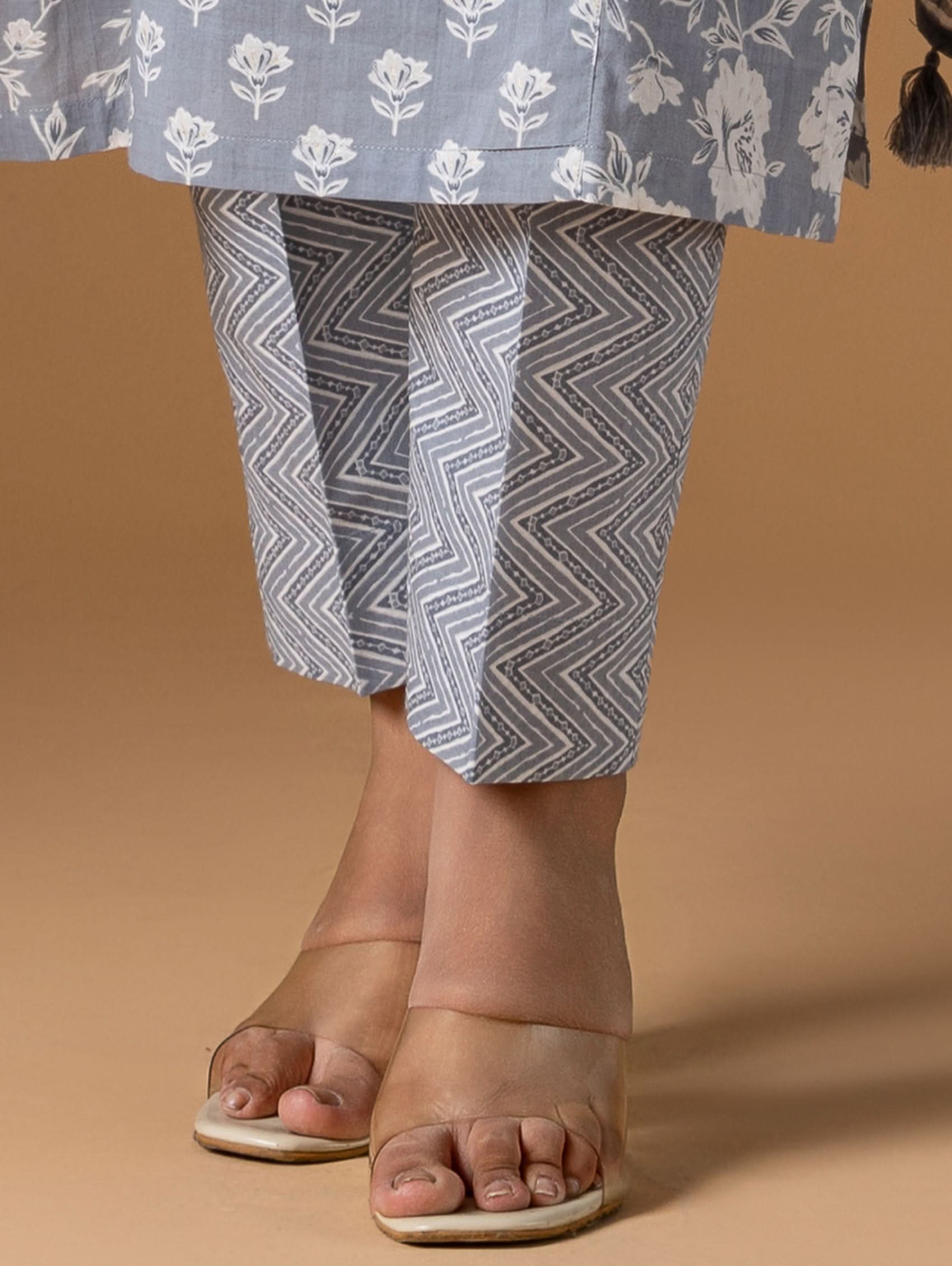 Person wearing a blue floral top and gray chevron-patterned pants on a beige background