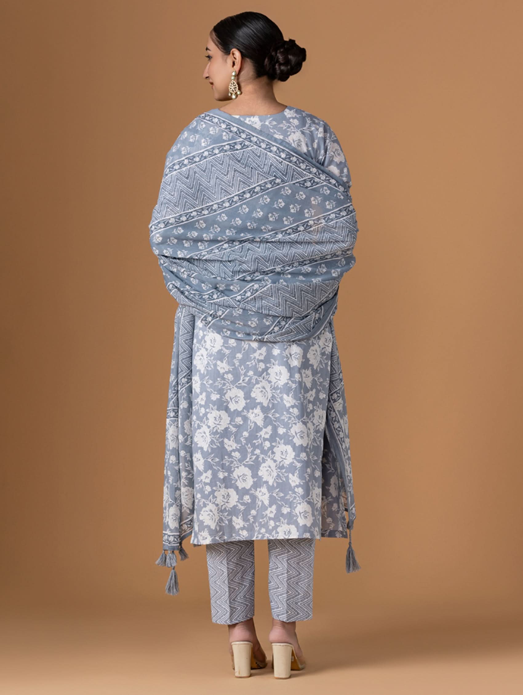 Woman wearing a gray patterned outfit with a matching shawl on a brown background