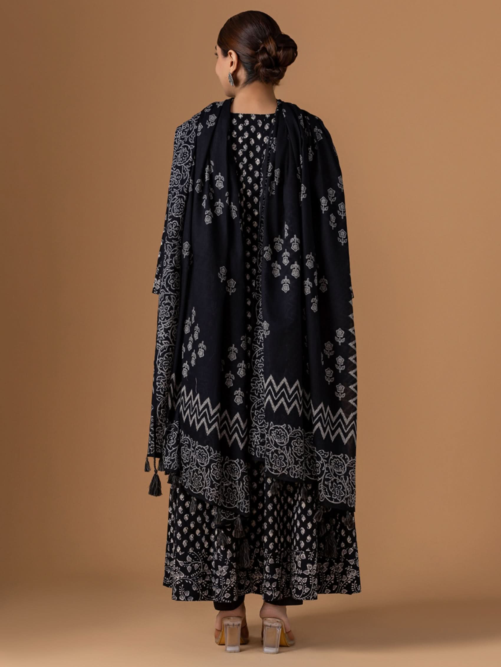 Woman wearing a black patterned outfit with a matching shawl on a brown background