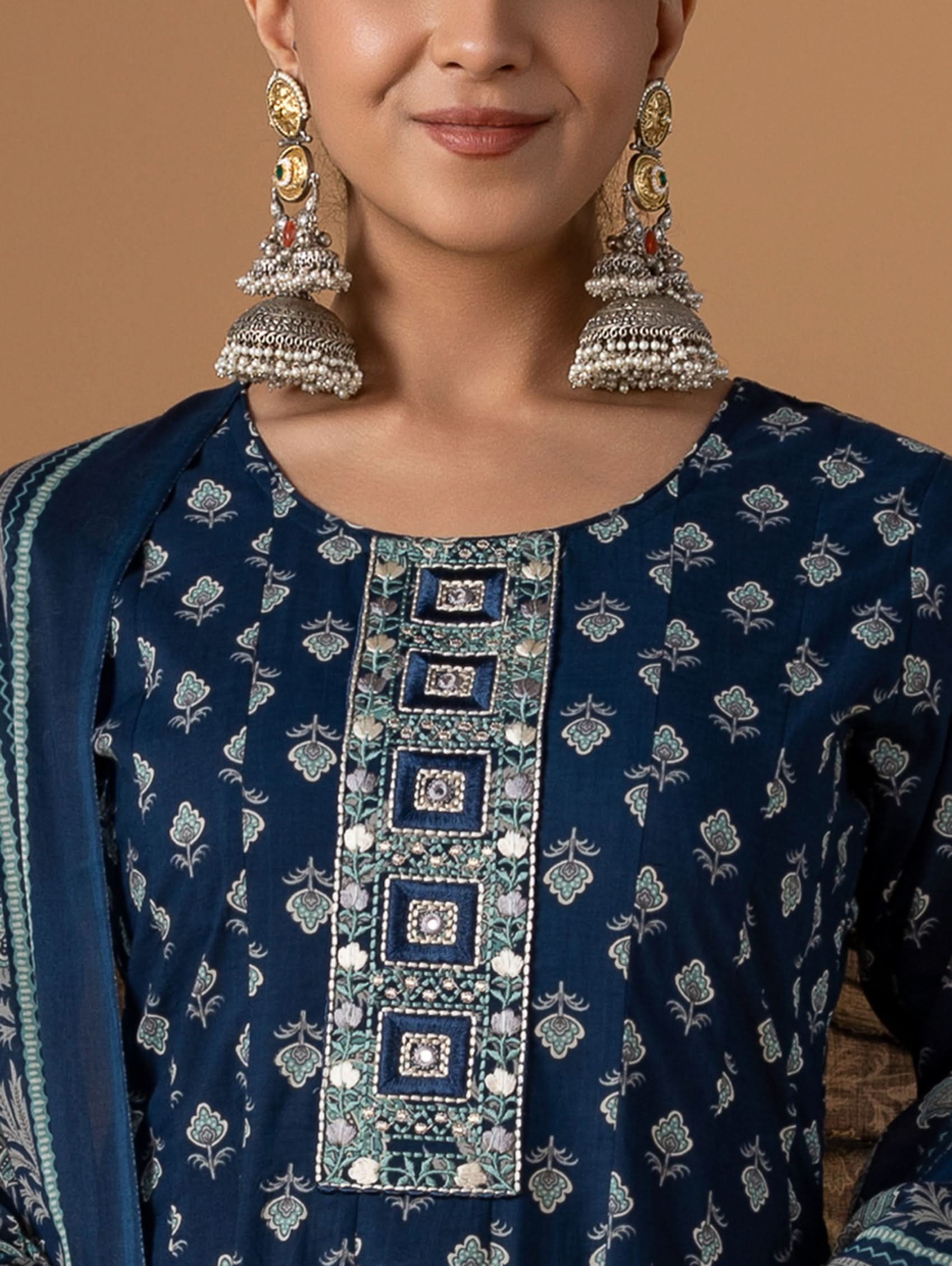 Woman wearing a blue embroidered outfit with silver earrings against a brown background