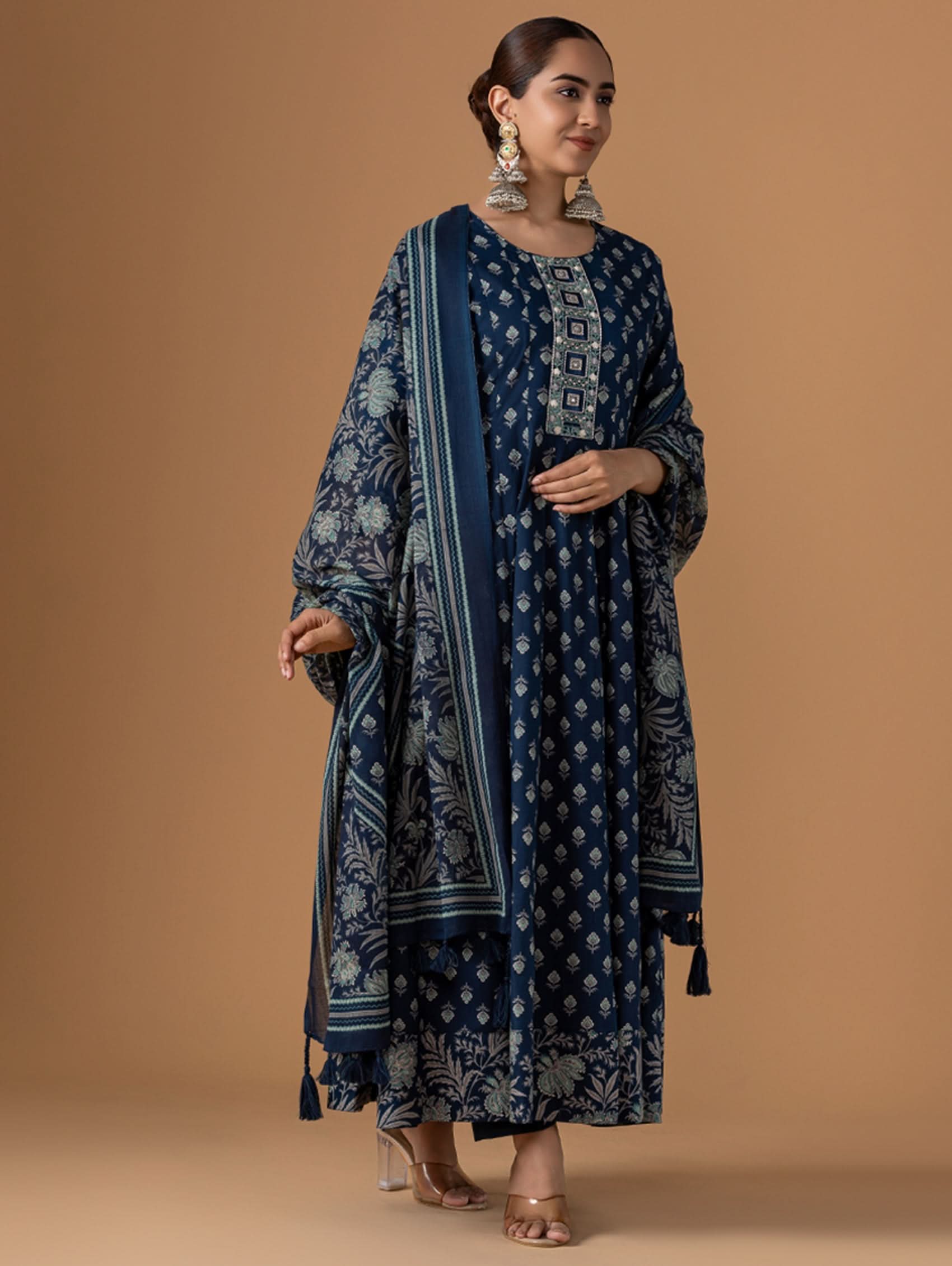 Woman wearing a blue patterned dress with a matching scarf against a brown background