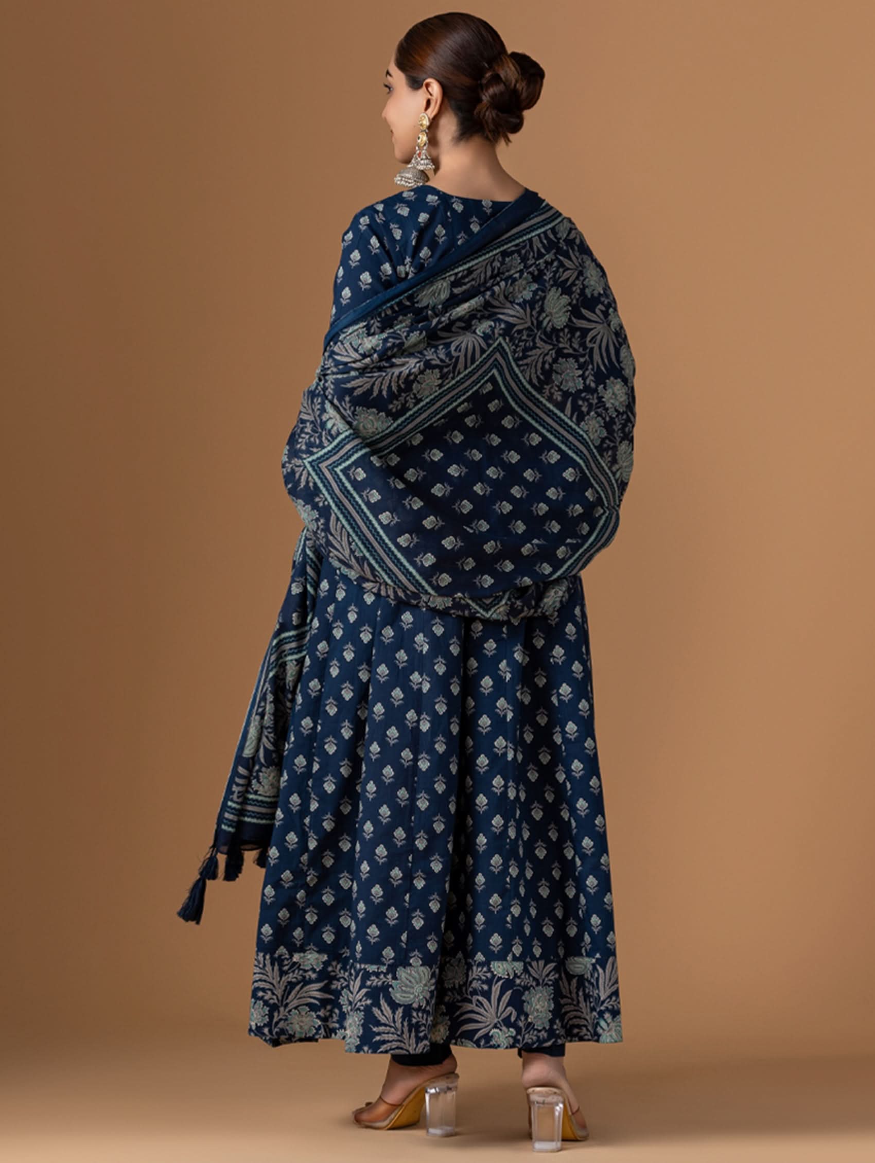 Woman wearing a blue patterned dress with a matching shawl against a brown background