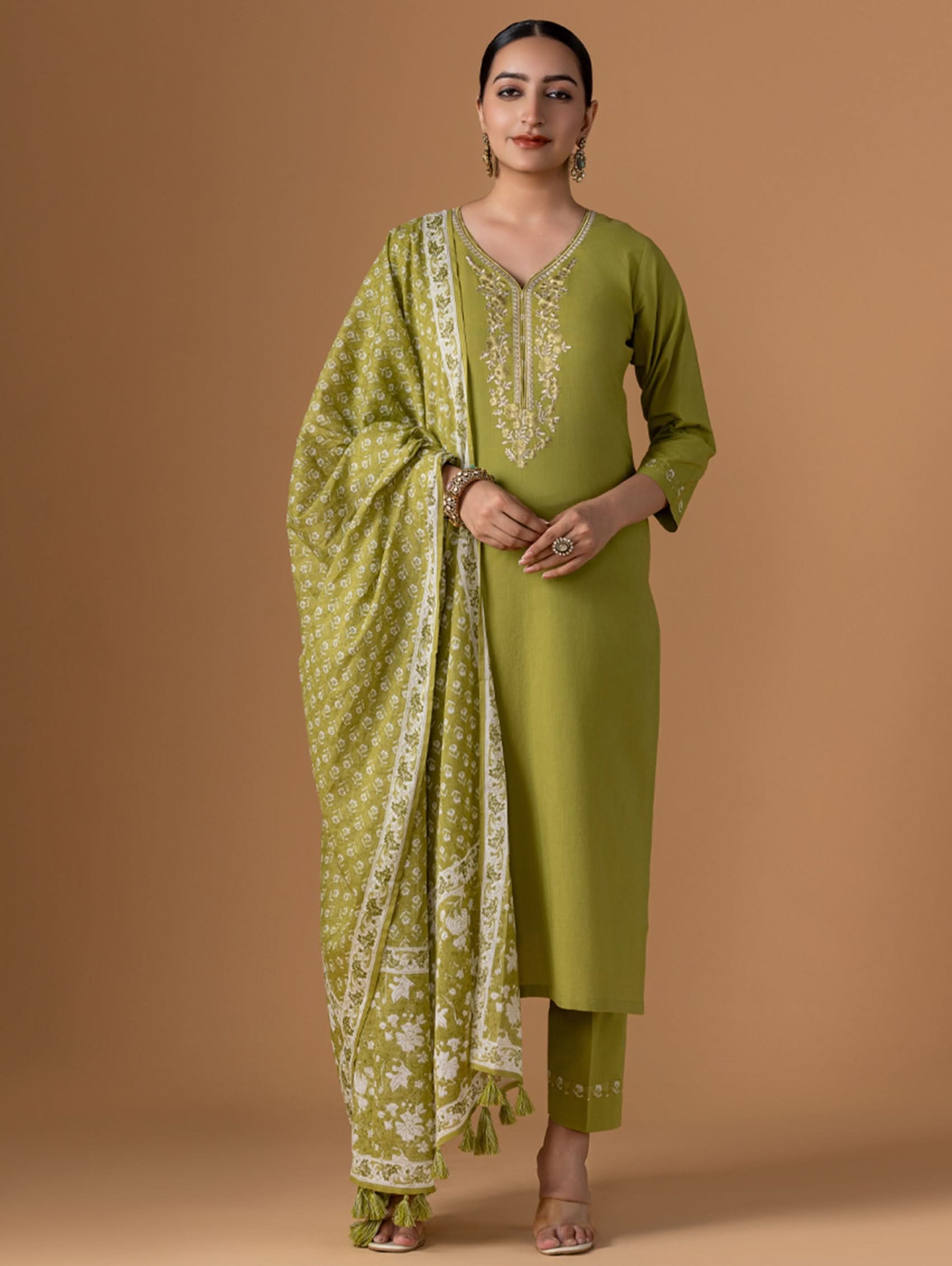 Woman wearing a green traditional outfit with a matching dupatta on a brown background