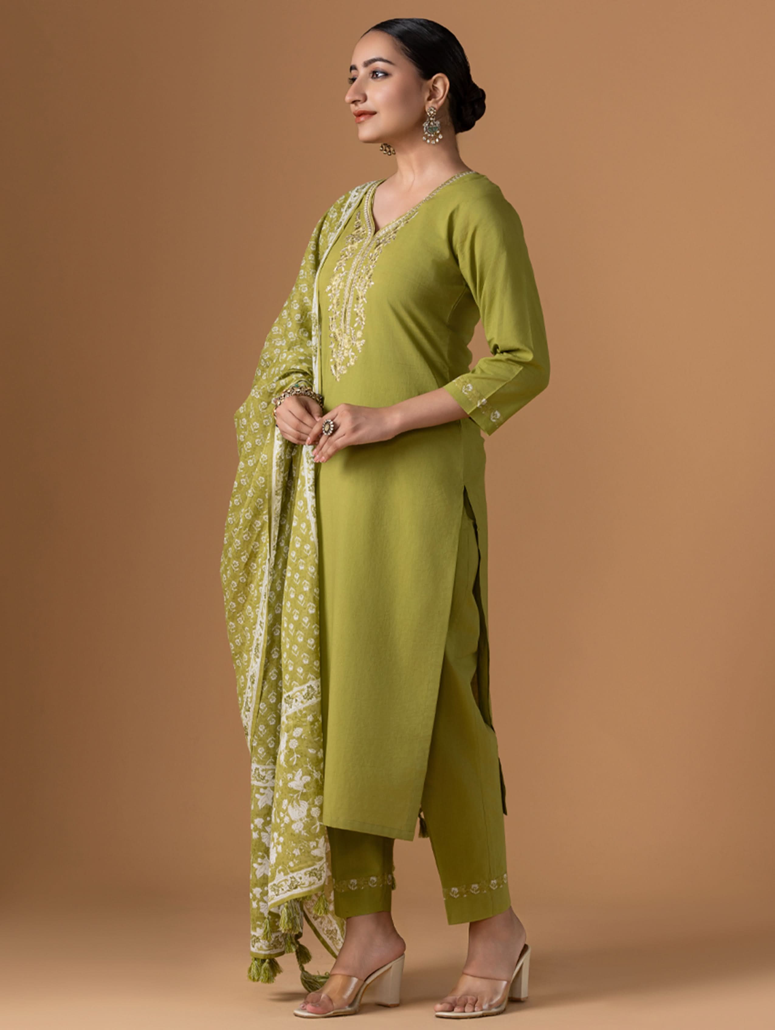 Woman wearing a green traditional outfit with a matching dupatta on a brown background