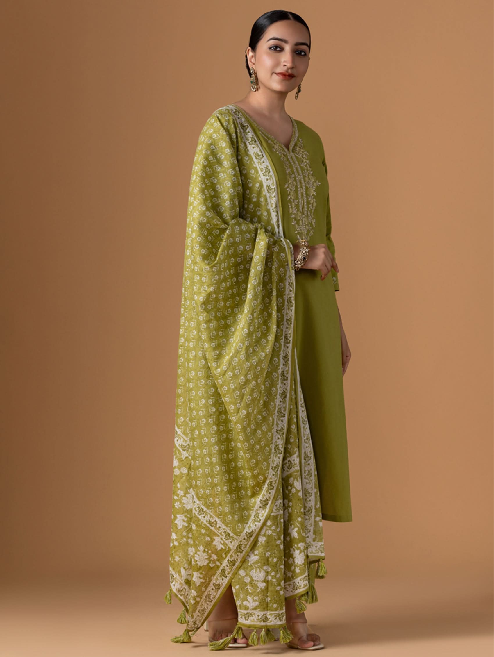 Woman wearing a green traditional outfit with a matching dupatta on a brown background