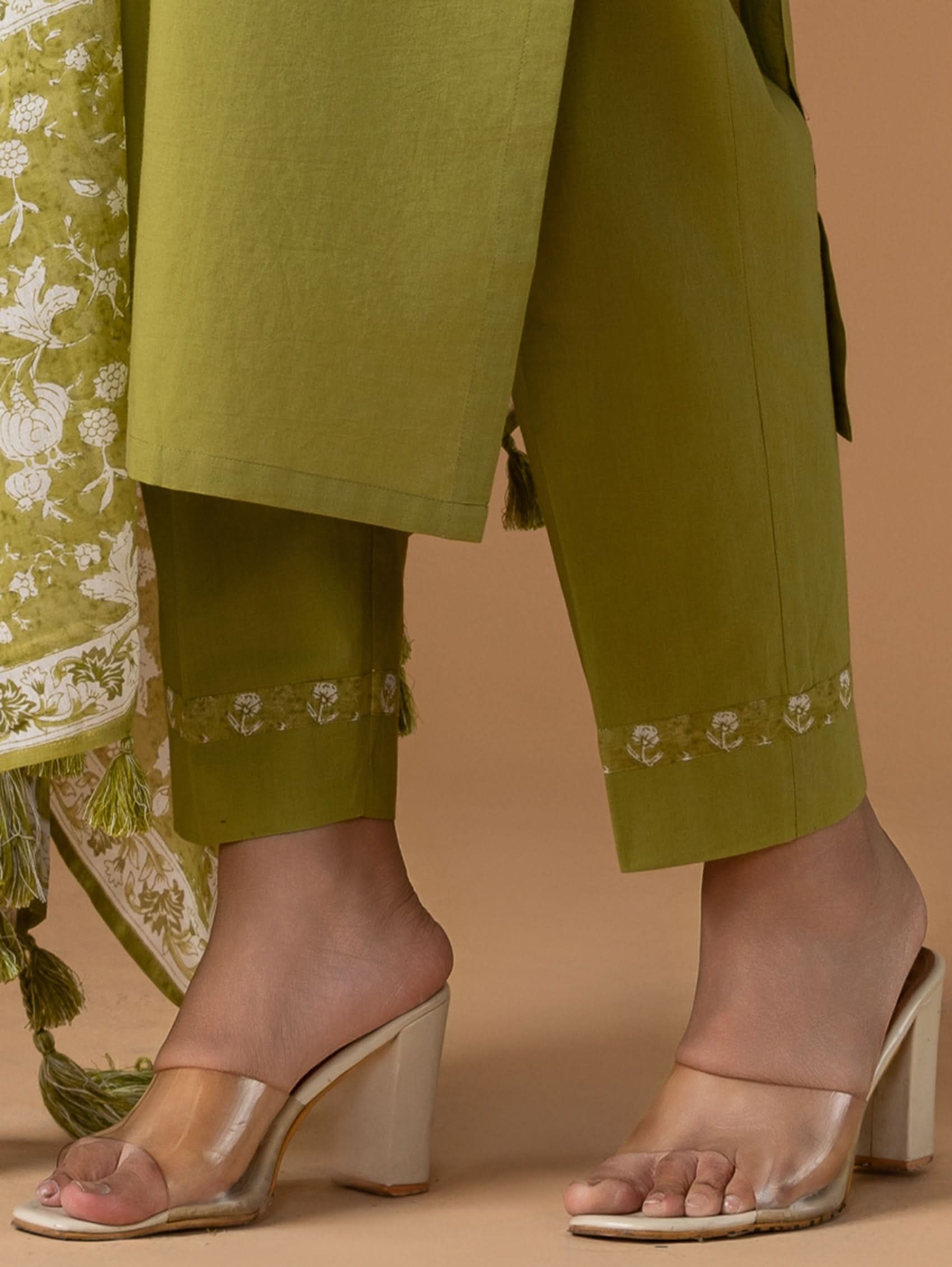 Green embroidered outfit with beige sandals on a beige background