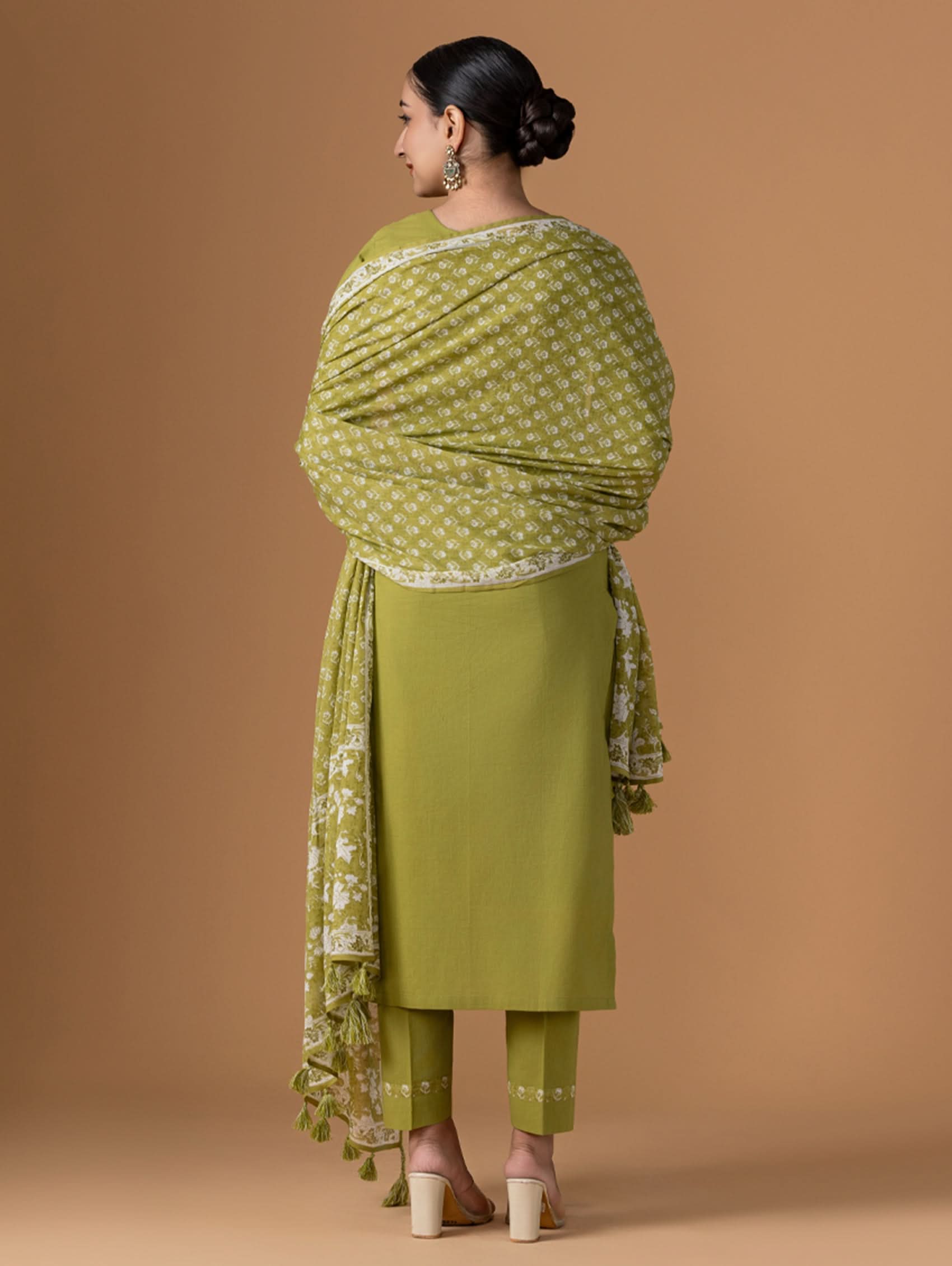 Woman wearing a green traditional outfit with a matching dupatta against a beige background