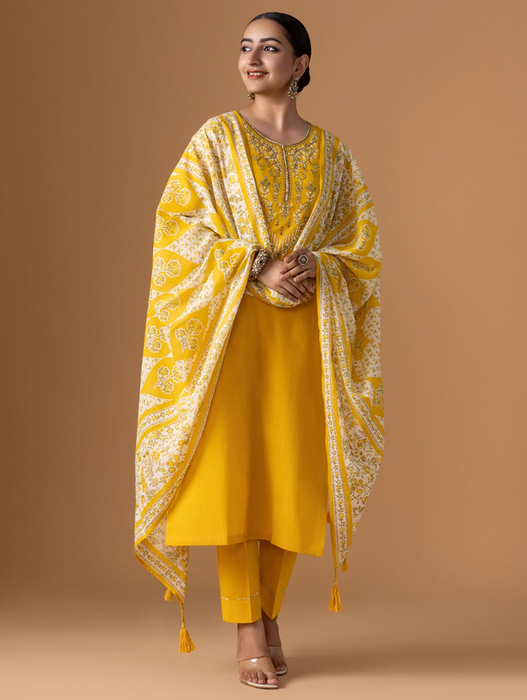 Woman wearing a yellow traditional outfit with a matching dupatta on a brown background