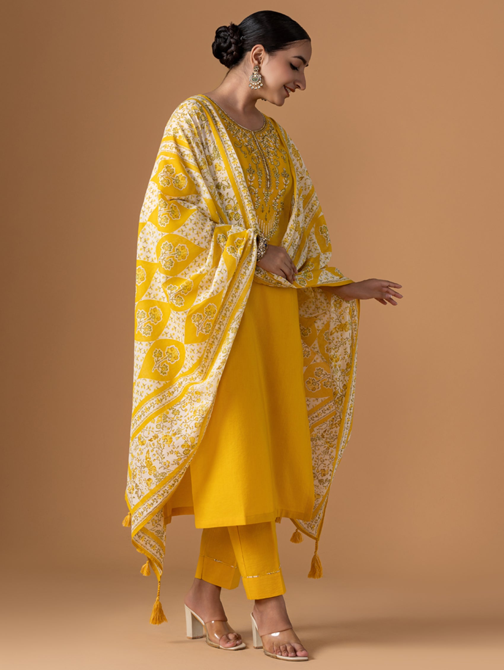 Woman wearing a yellow traditional outfit with a matching dupatta on a beige background