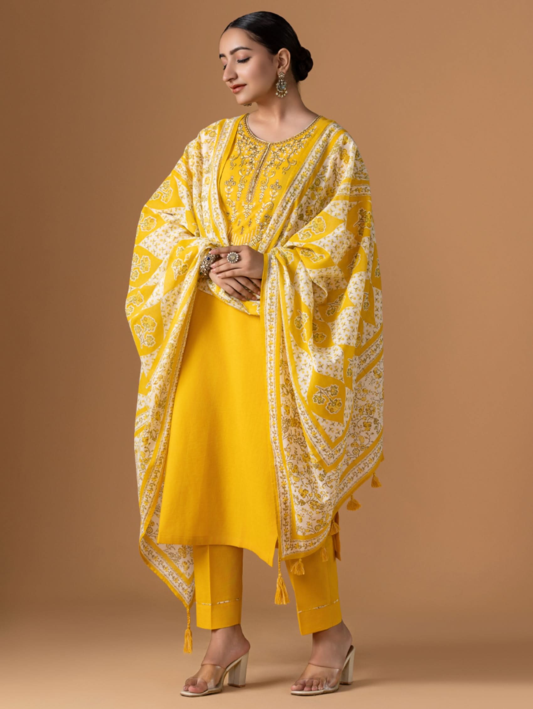 Woman wearing a yellow traditional outfit with a matching dupatta on a brown background