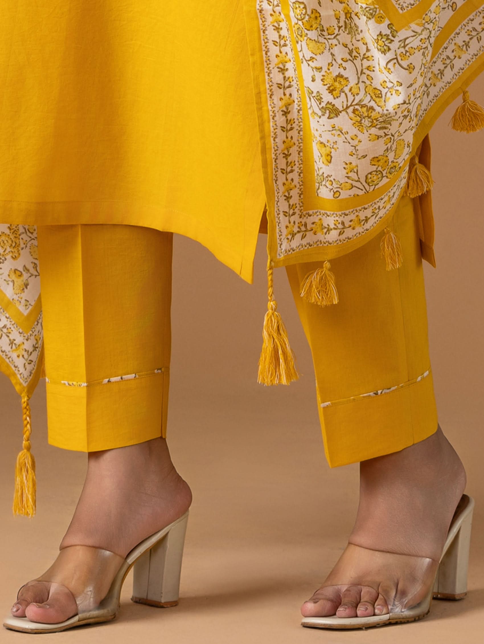 Yellow traditional outfit with floral patterns and tassels on a beige background
