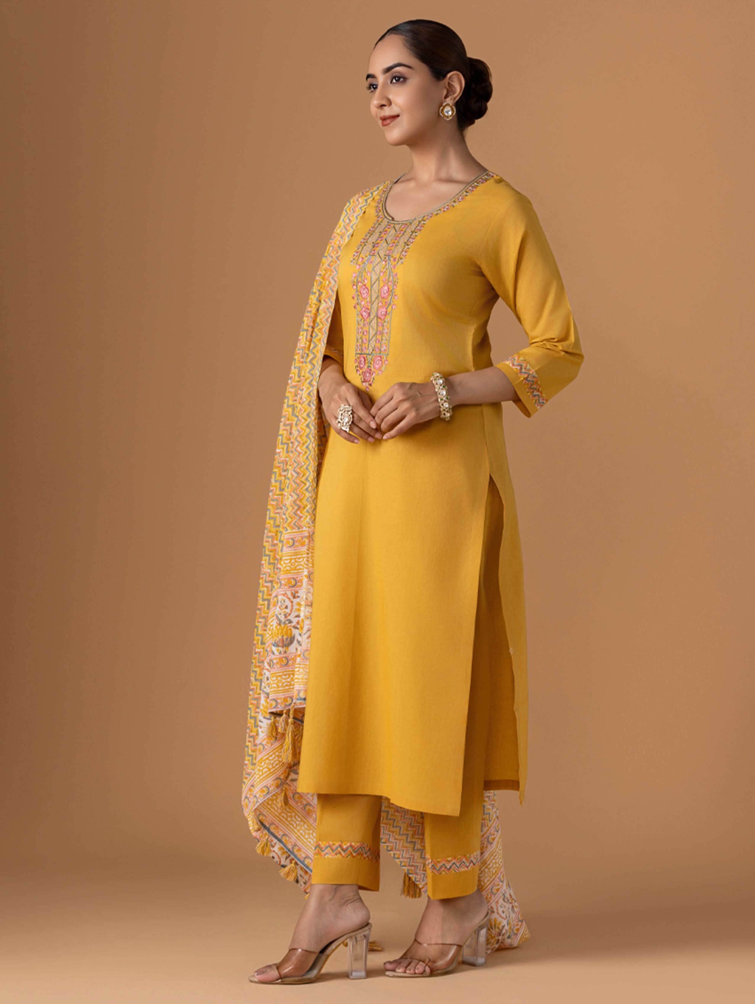 Woman wearing a yellow traditional outfit with a matching dupatta on a beige background