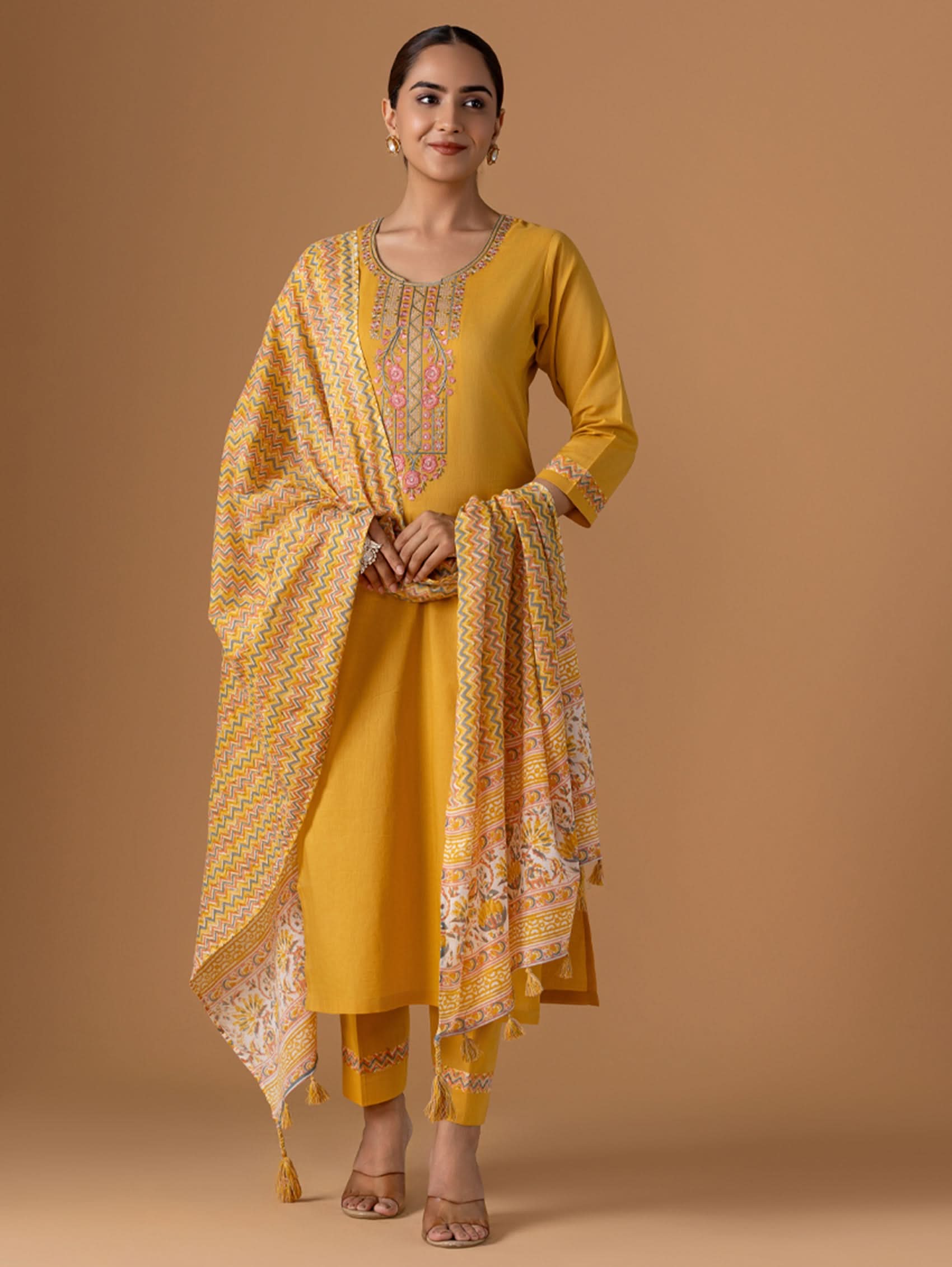Woman wearing a yellow traditional outfit with a matching dupatta on a brown background