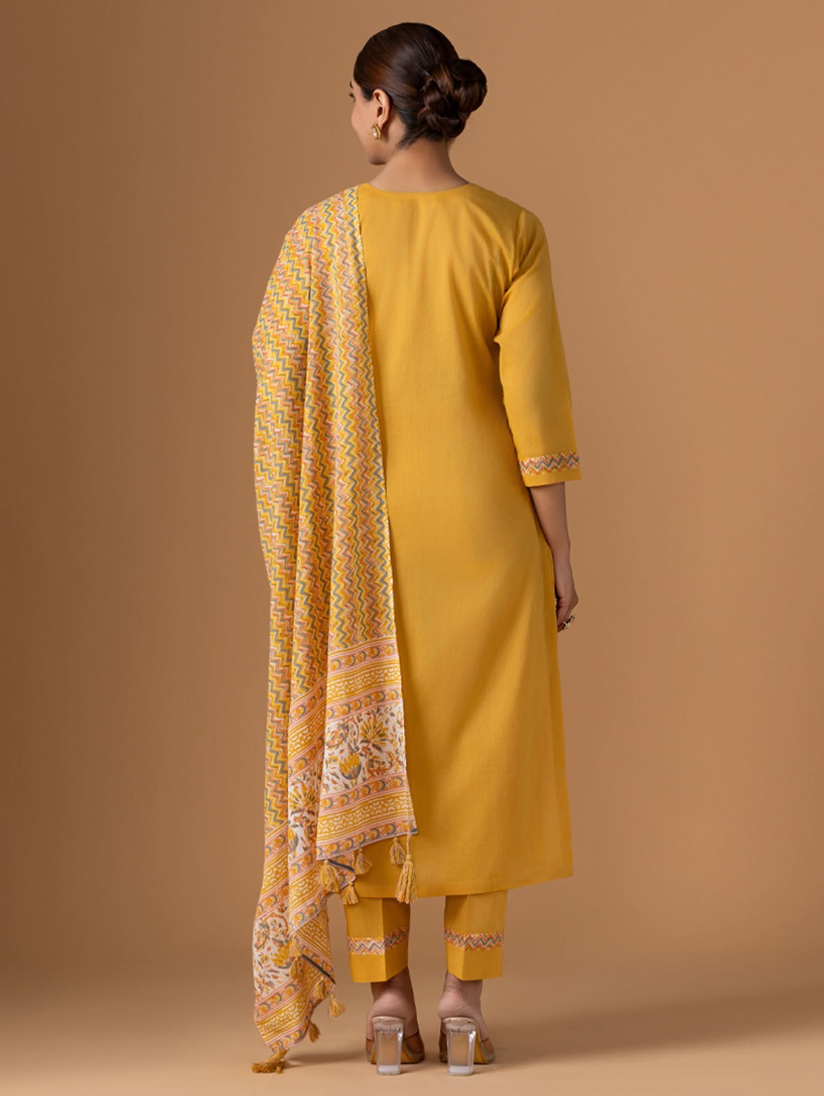 Woman wearing a yellow outfit with a patterned scarf on a brown background
