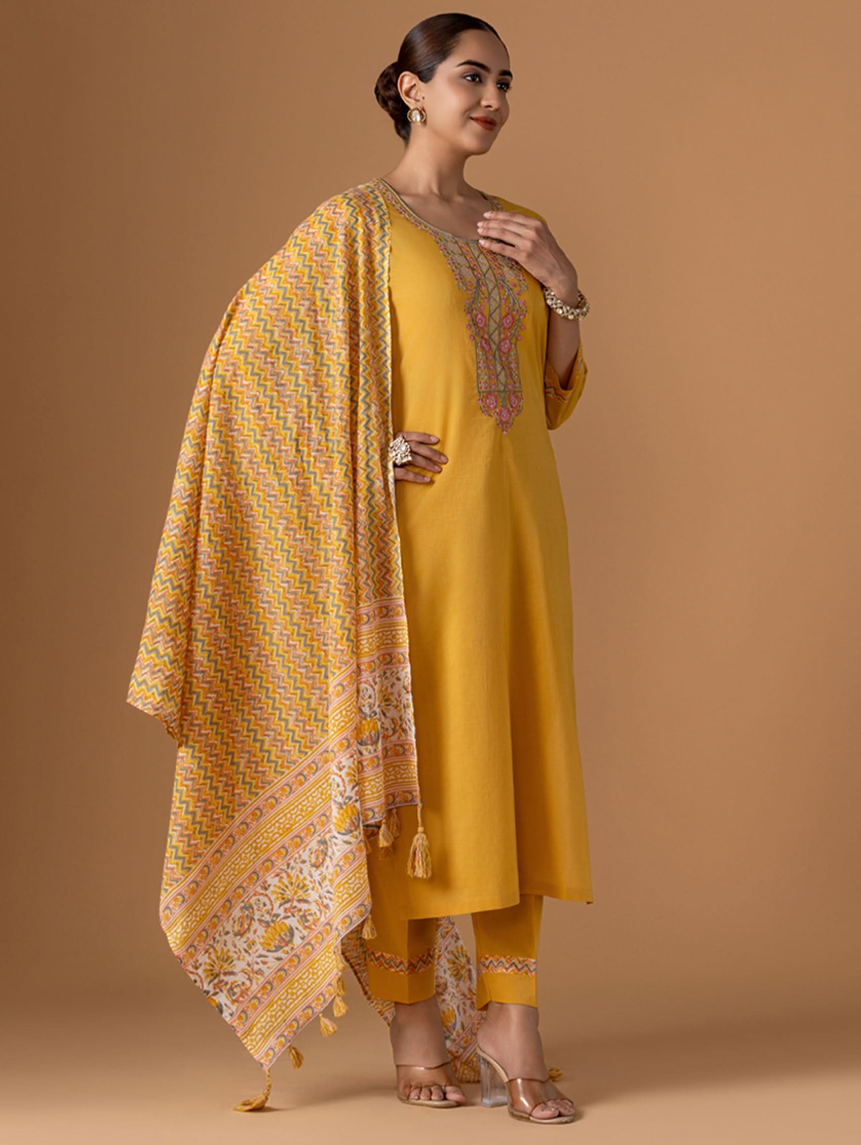 Woman wearing a yellow traditional outfit with a matching dupatta on a brown background