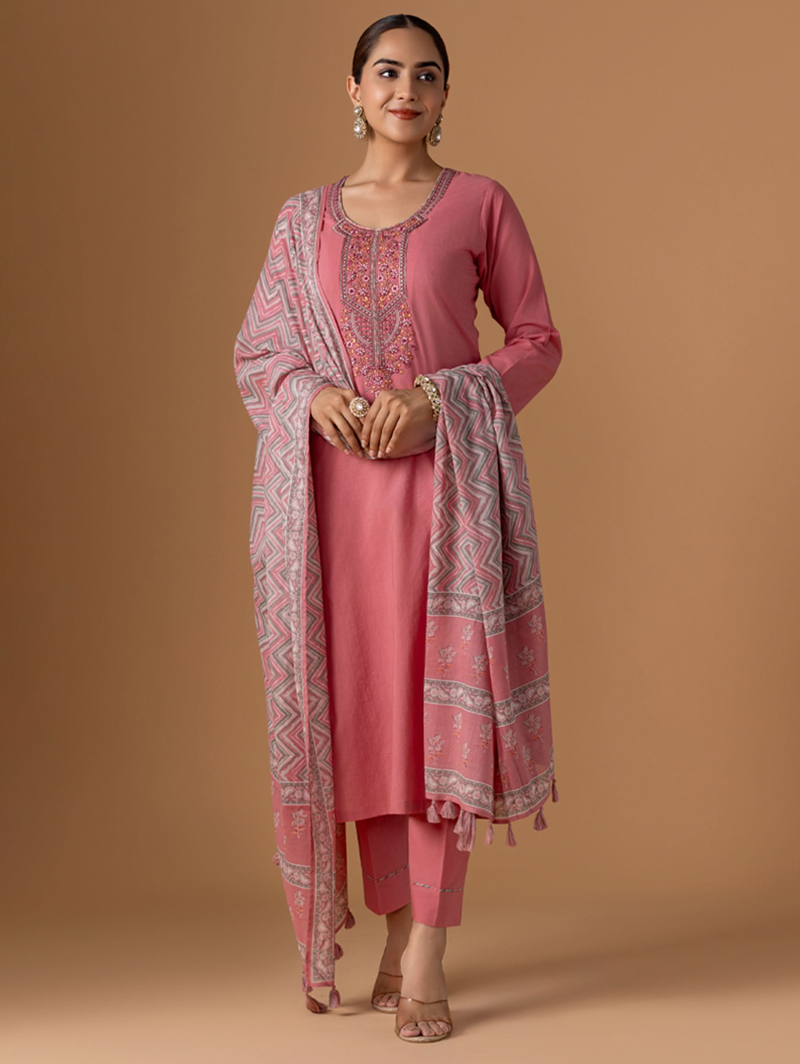 Woman wearing a pink traditional outfit with a matching dupatta on a beige background