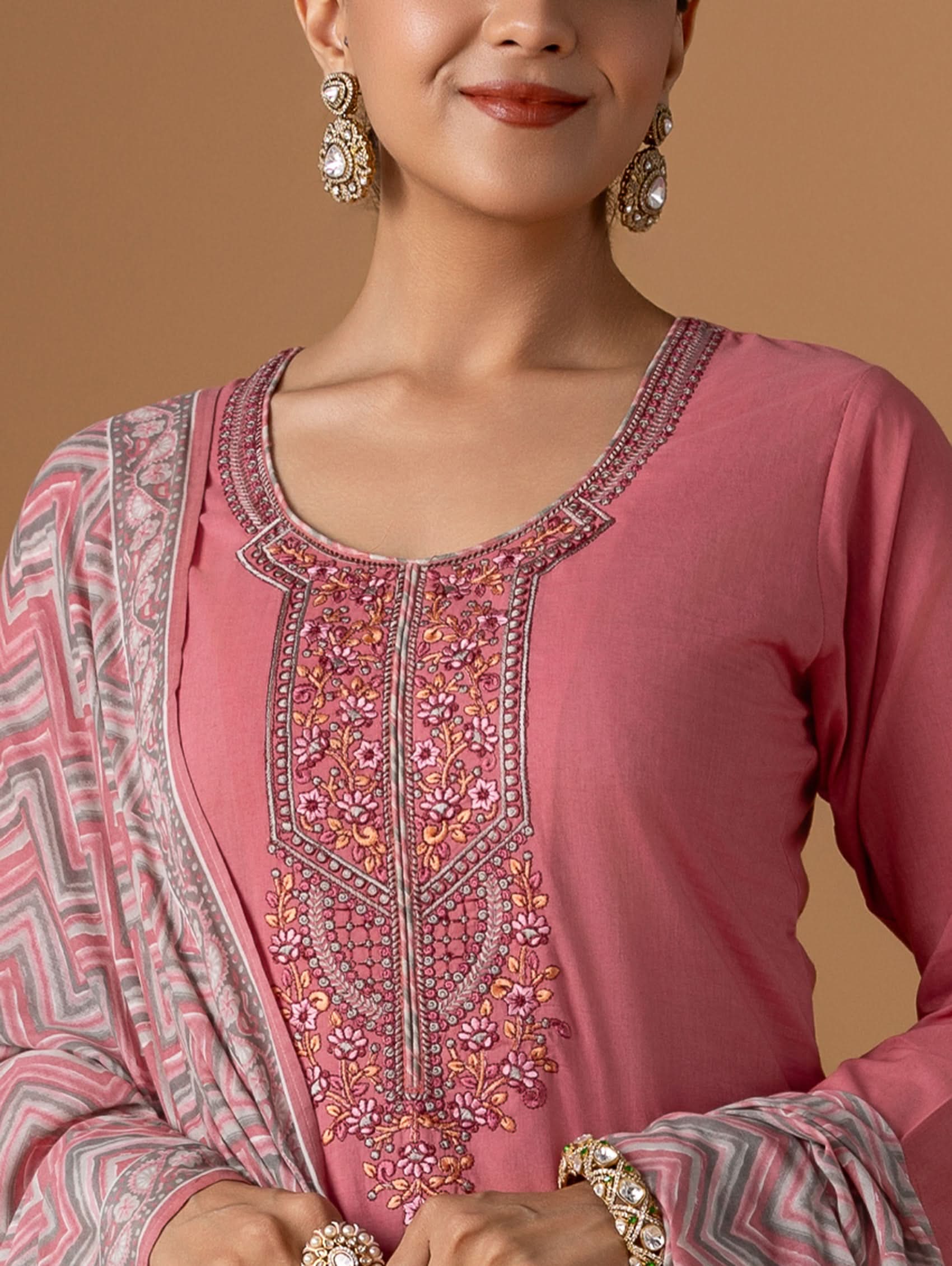Woman wearing a pink embroidered traditional outfit with a beige background