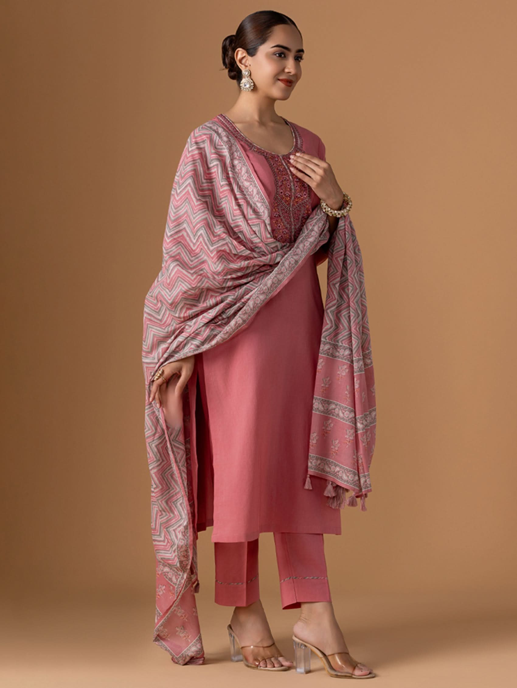 Woman wearing a pink traditional outfit with a patterned shawl on a beige background
