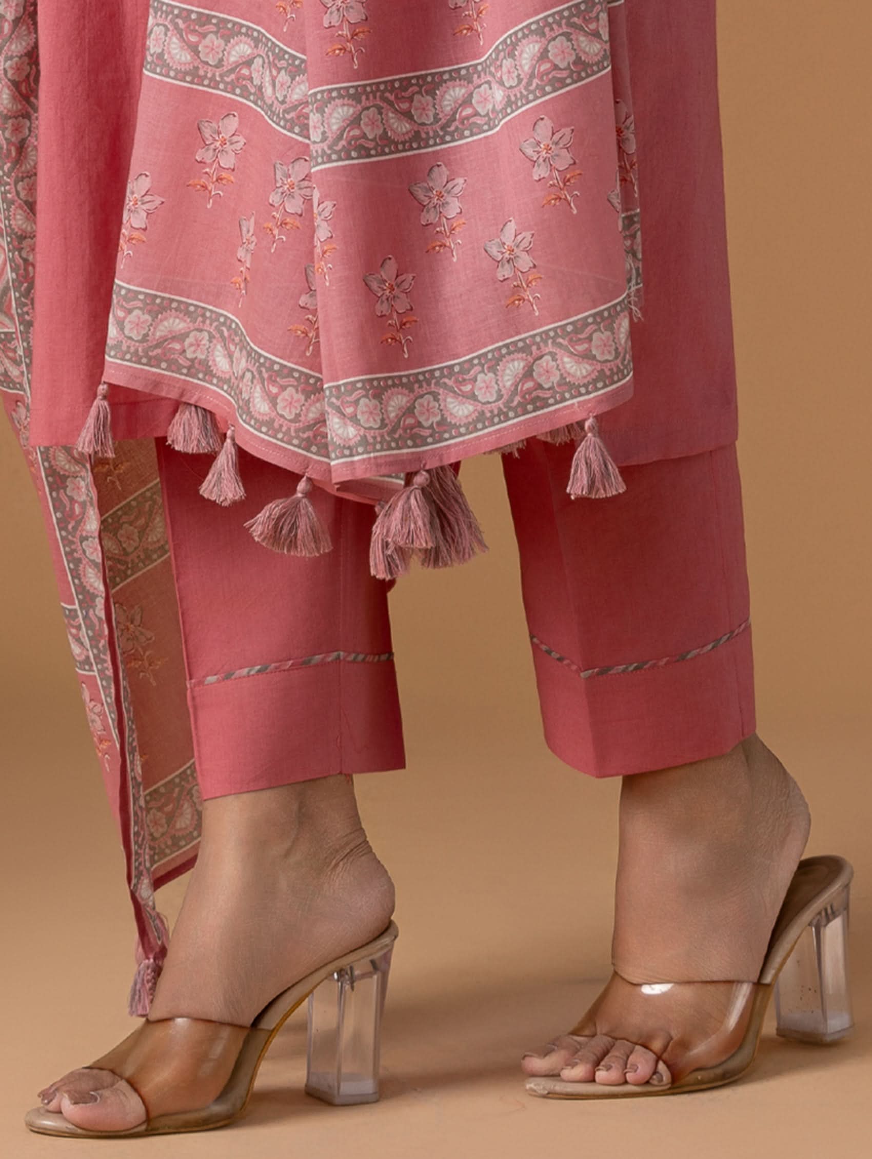 Pink traditional outfit with floral patterns and tassels on a beige background