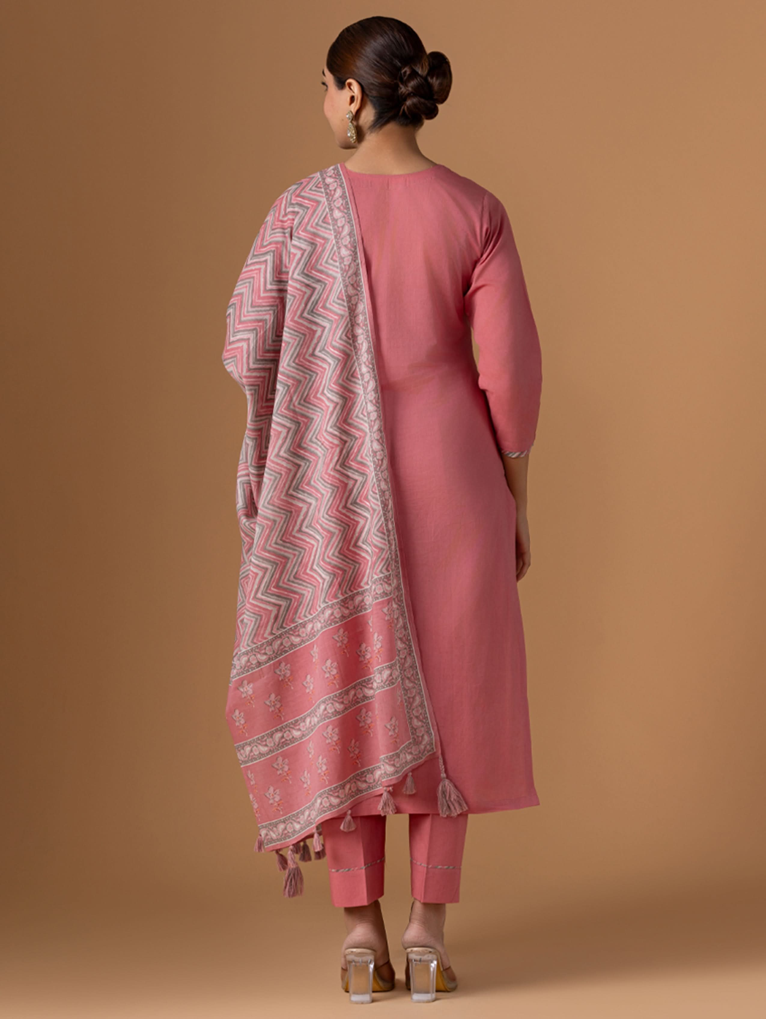 Woman wearing a pink traditional outfit with a patterned shawl on a brown background