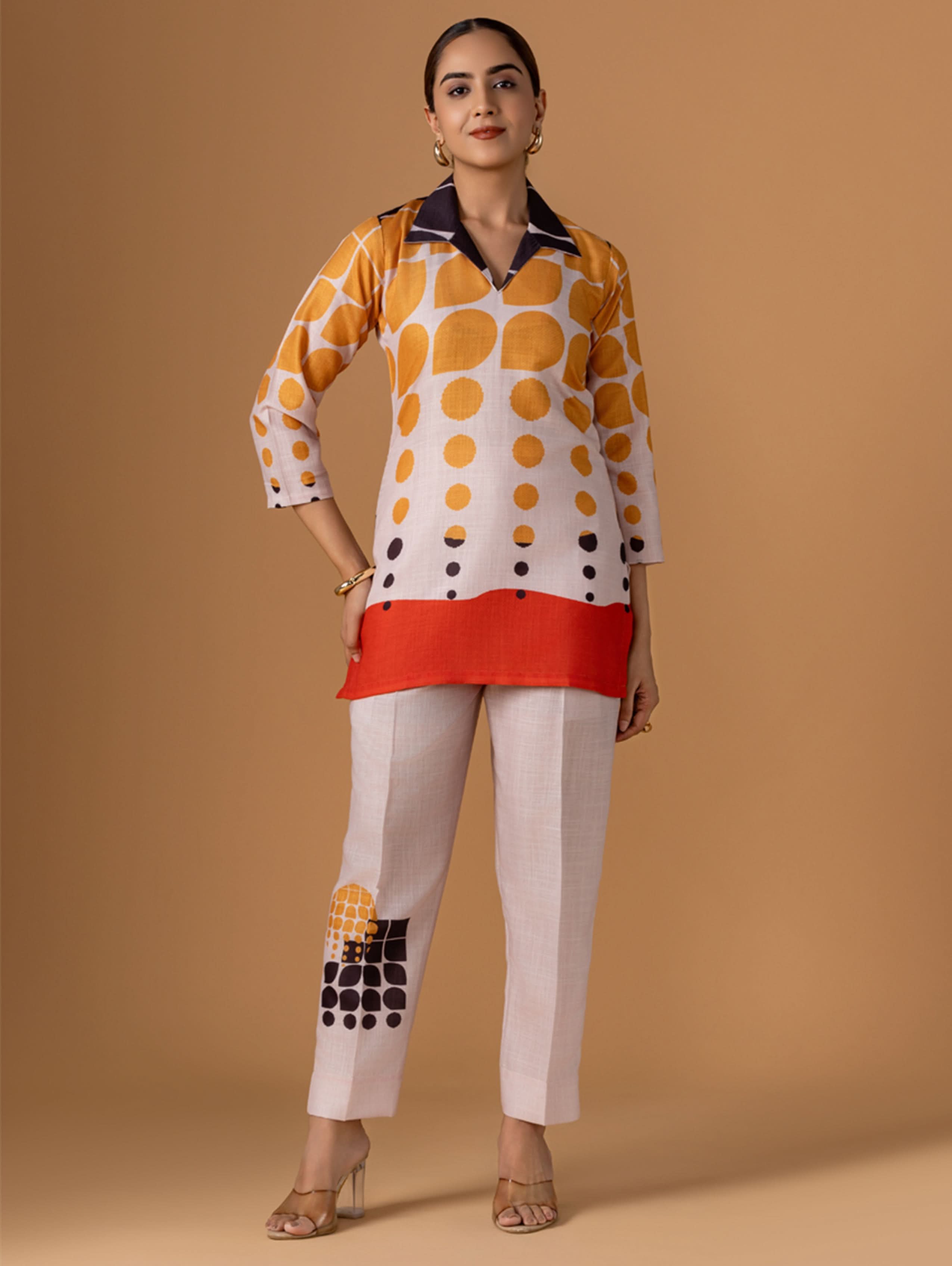 A woman modeling a digitally printed viscose silk co-ord set with a short kurta in multicolor geometric pattern and regular pants, paired with a red scarf.