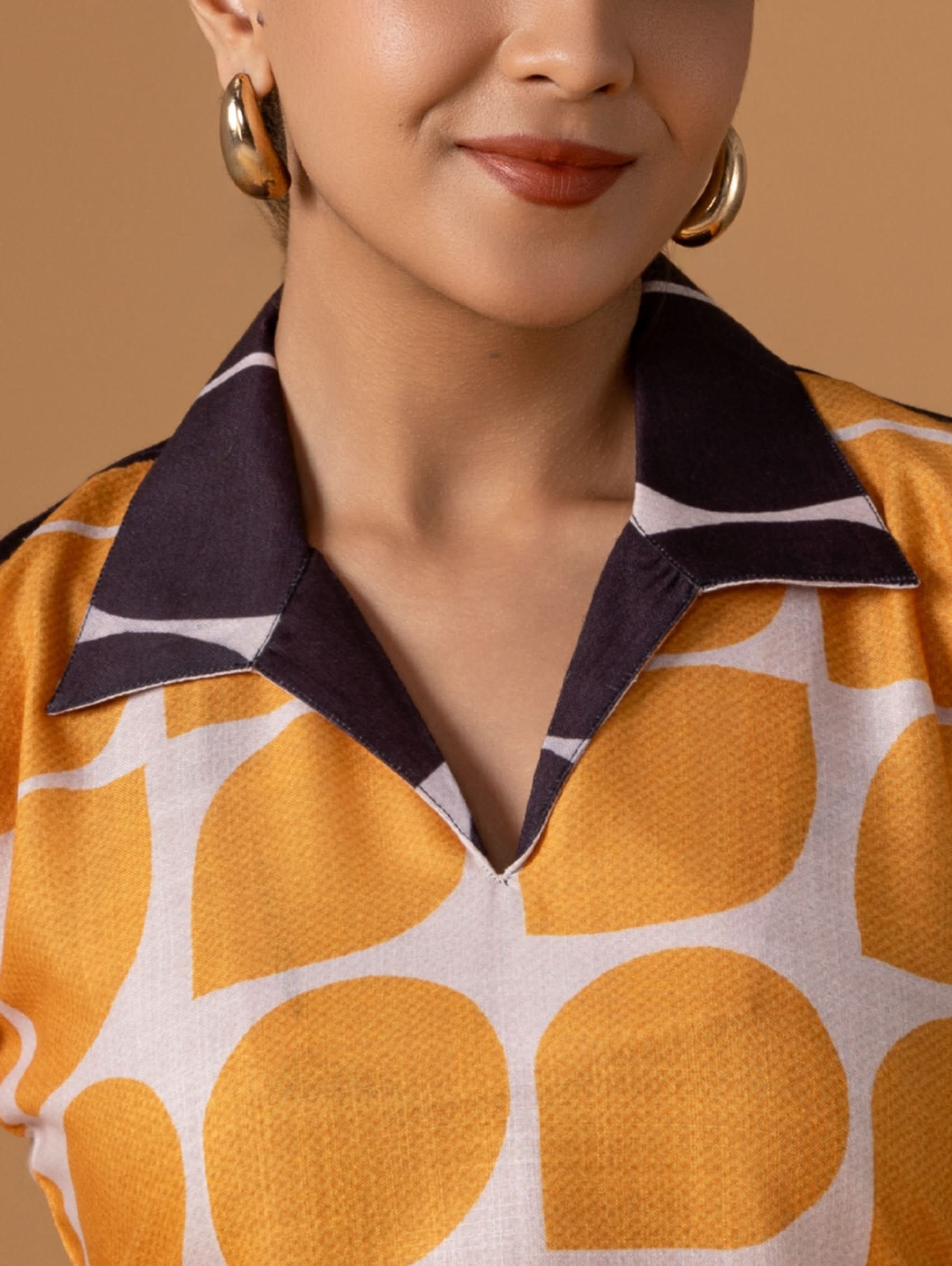 Close-up of a person wearing a patterned shirt with large orange shapes on a beige background