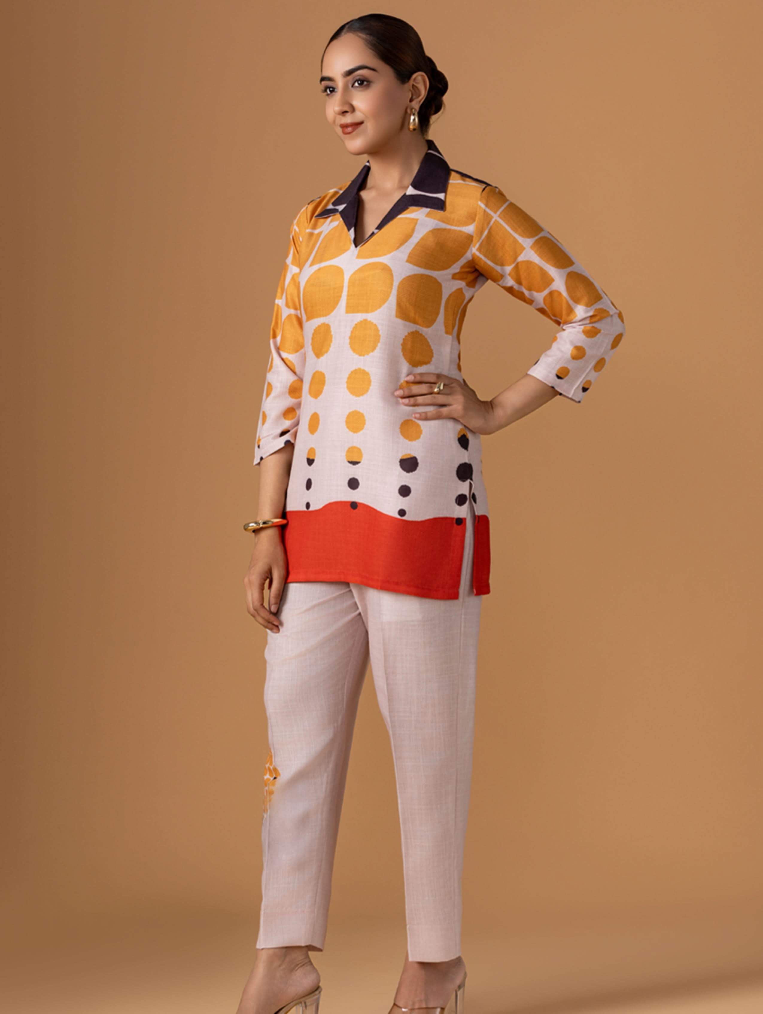 Woman wearing a patterned top and beige pants on a brown background