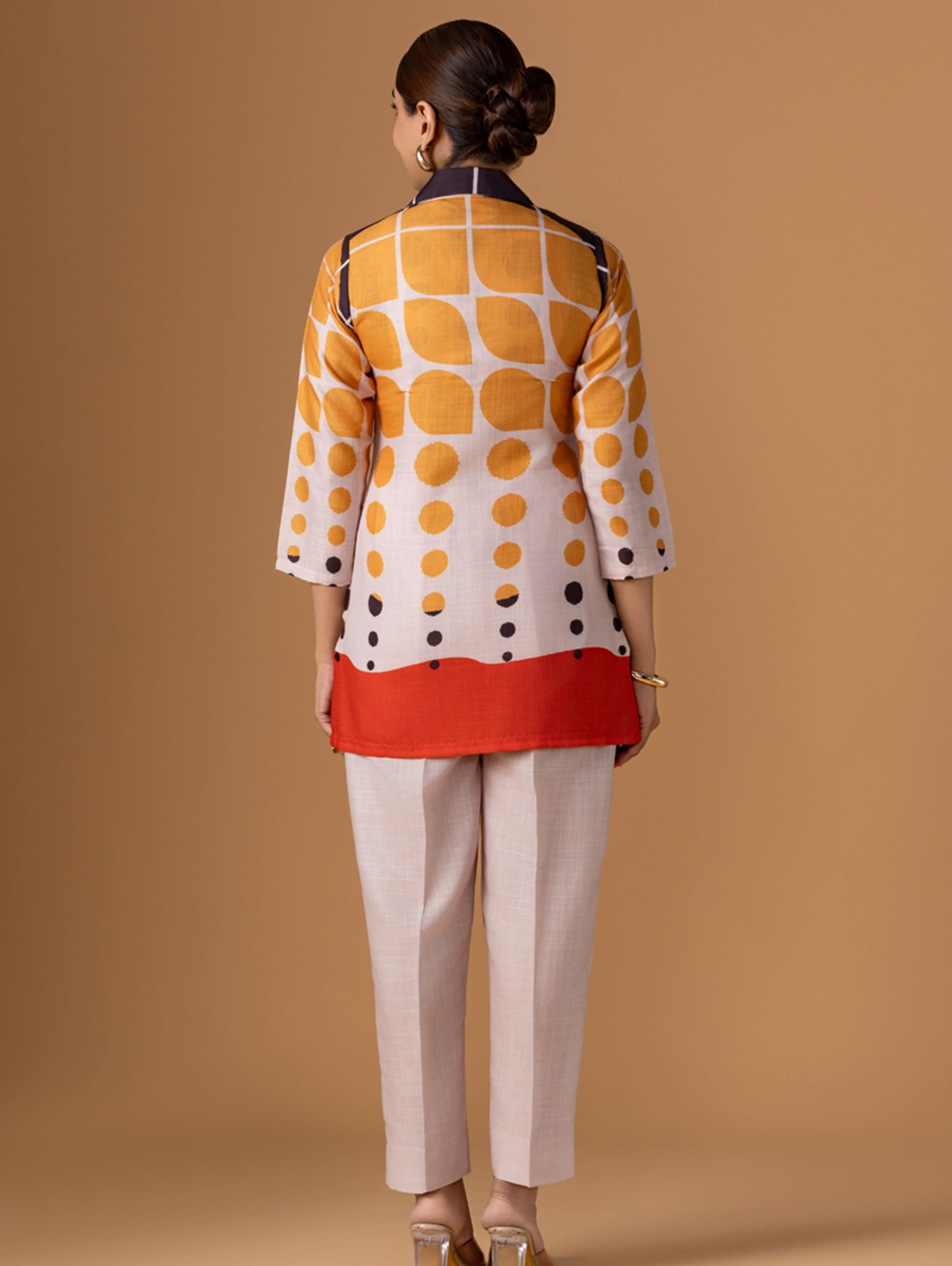Woman wearing a patterned jacket and beige pants on a brown background