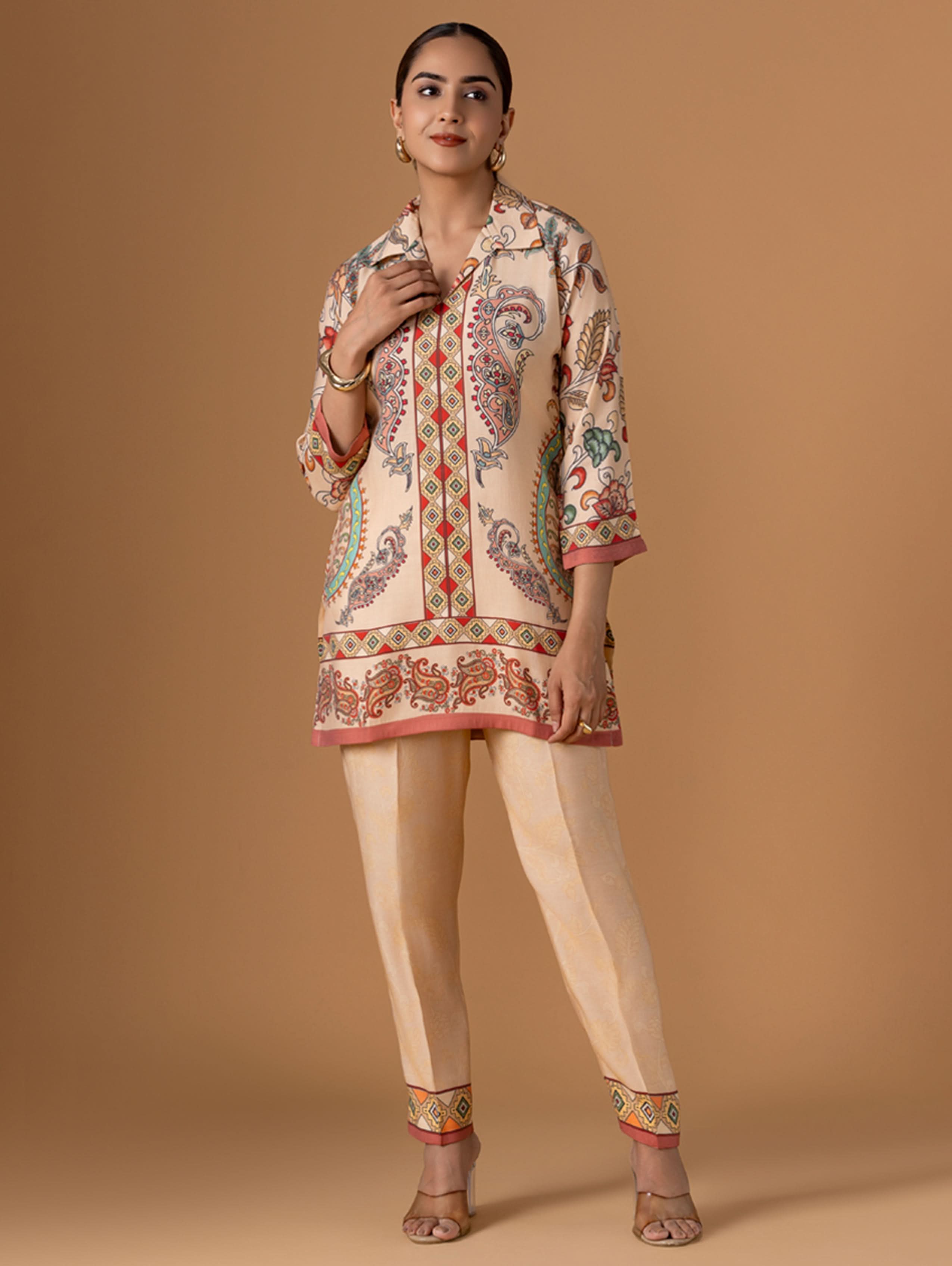 Woman wearing a patterned kurta with beige pants on a brown background