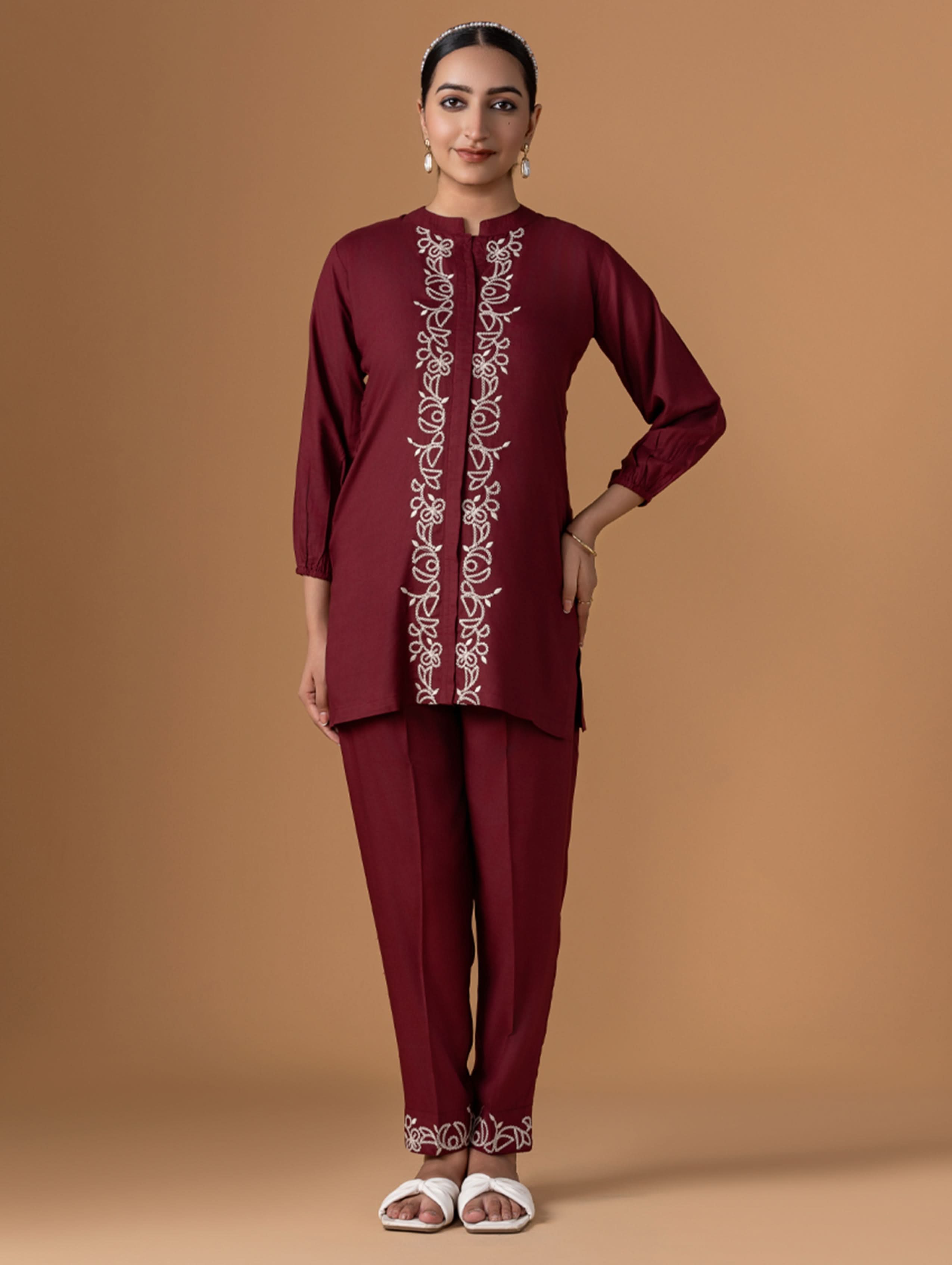 Woman wearing a maroon embroidered outfit on a brown background