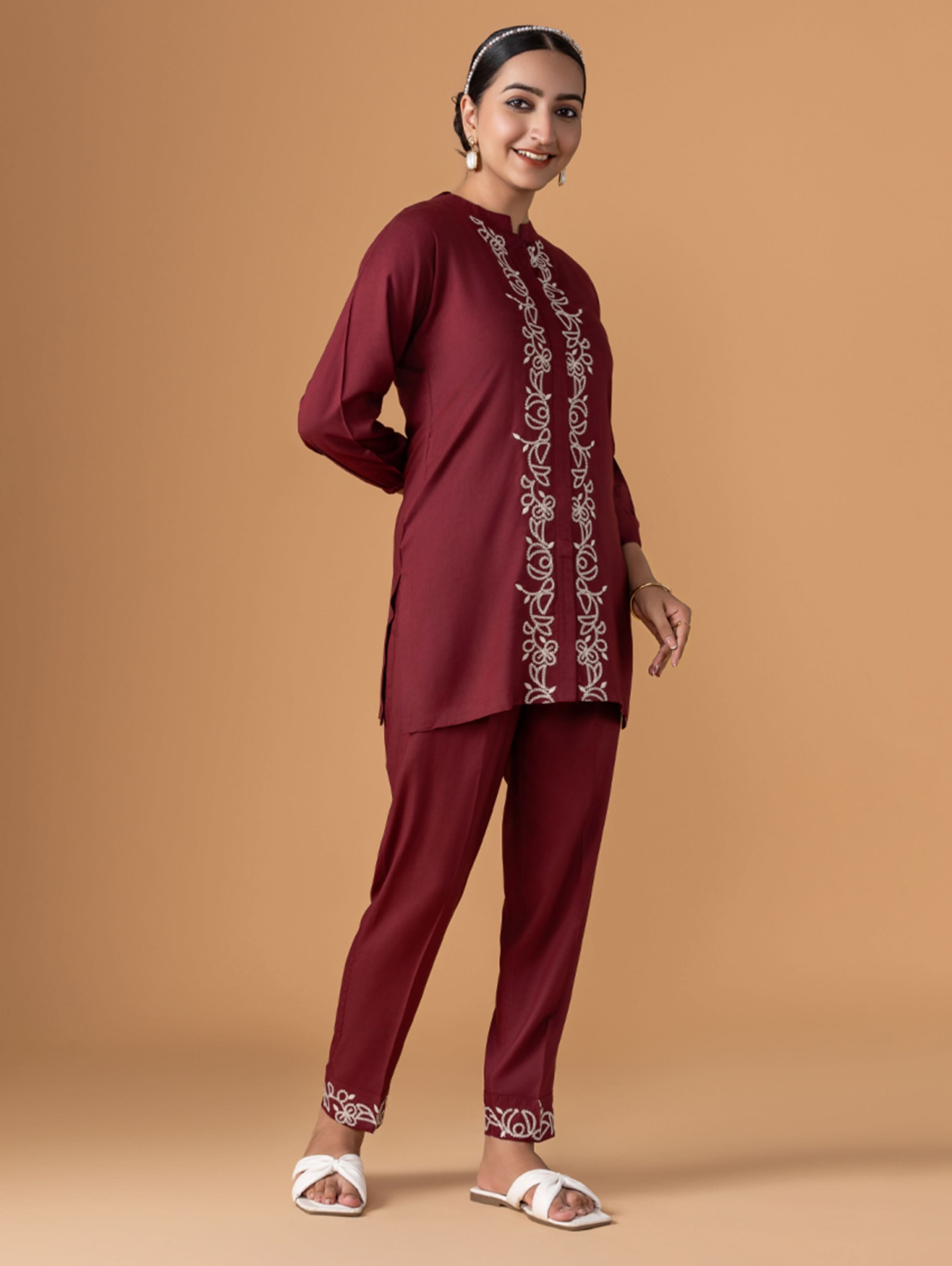 Woman wearing a maroon traditional outfit with embroidery on a beige background