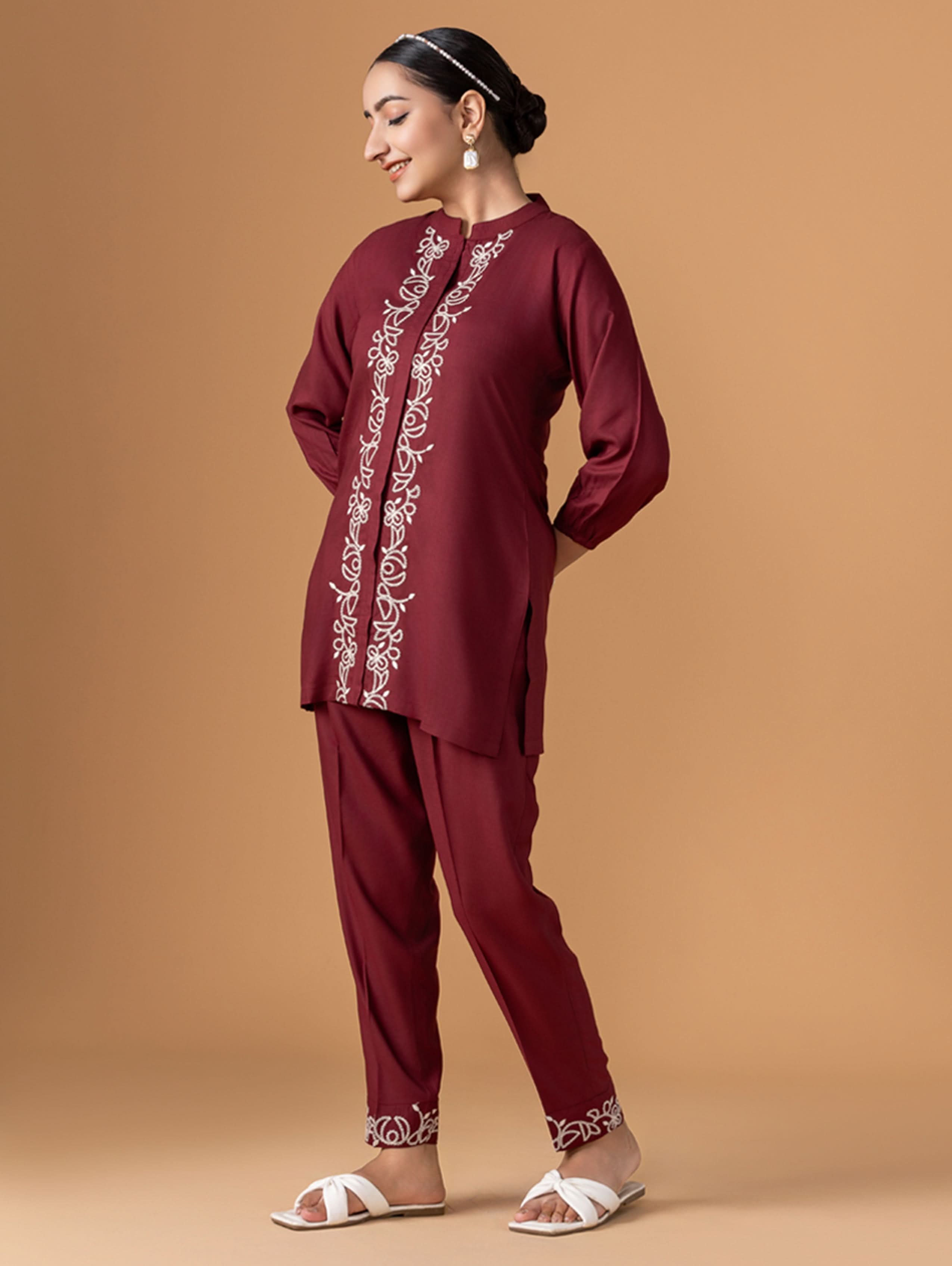 Woman wearing a maroon traditional outfit with white embroidery on a beige background